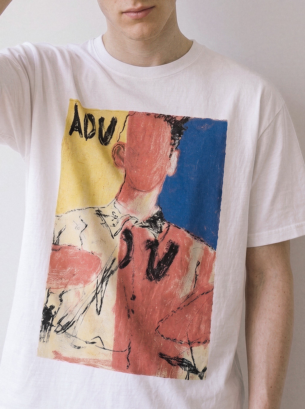 A male model posing wearing a white abstract faceless portrait graphic tee, capturing the tension of the unspoken identity visual statement.