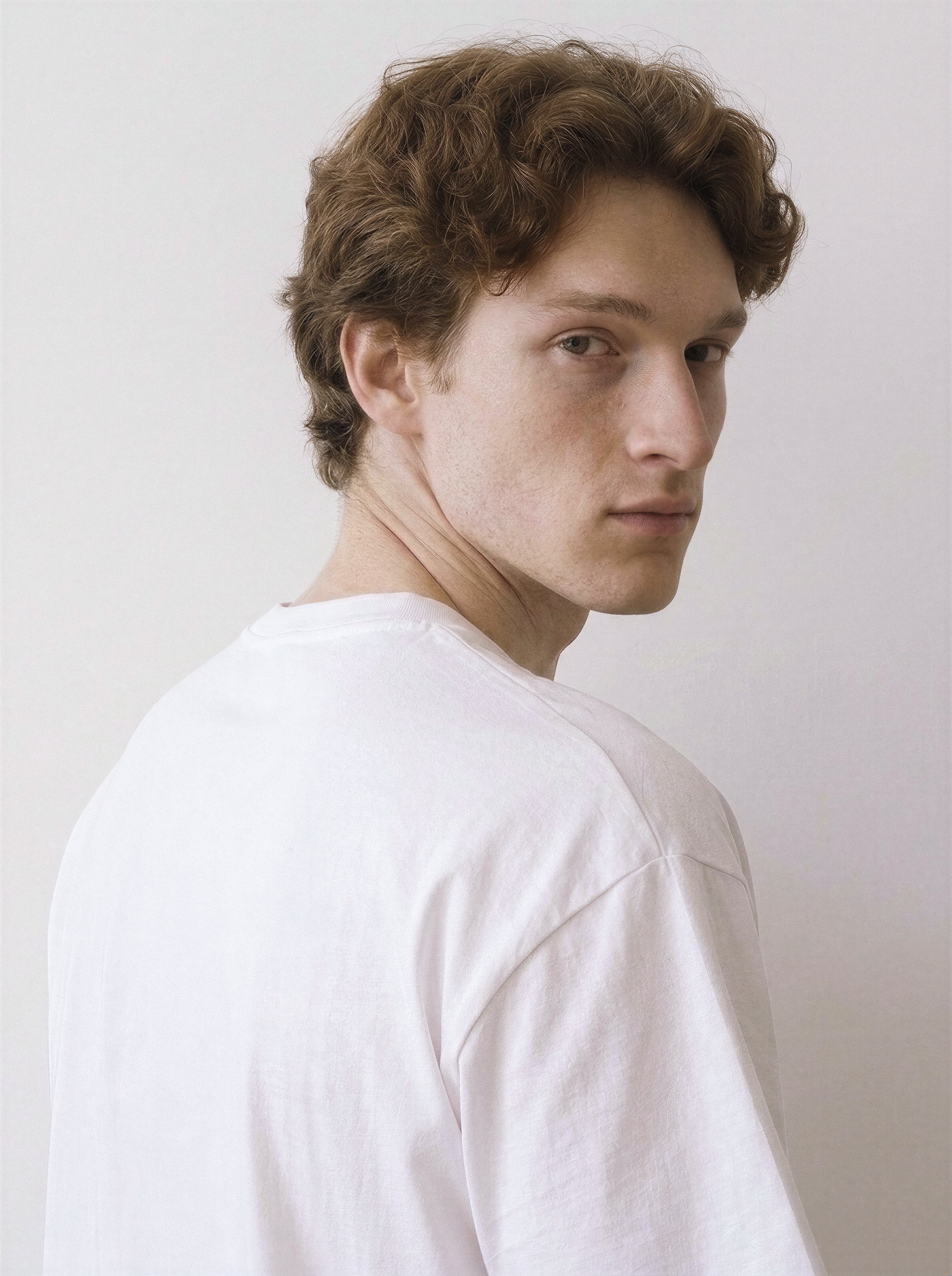 A back and shoulder view of a male model wearing a white abstract one-eye face line art graphic tee, demonstrating the garment's drape and striking line art style.
