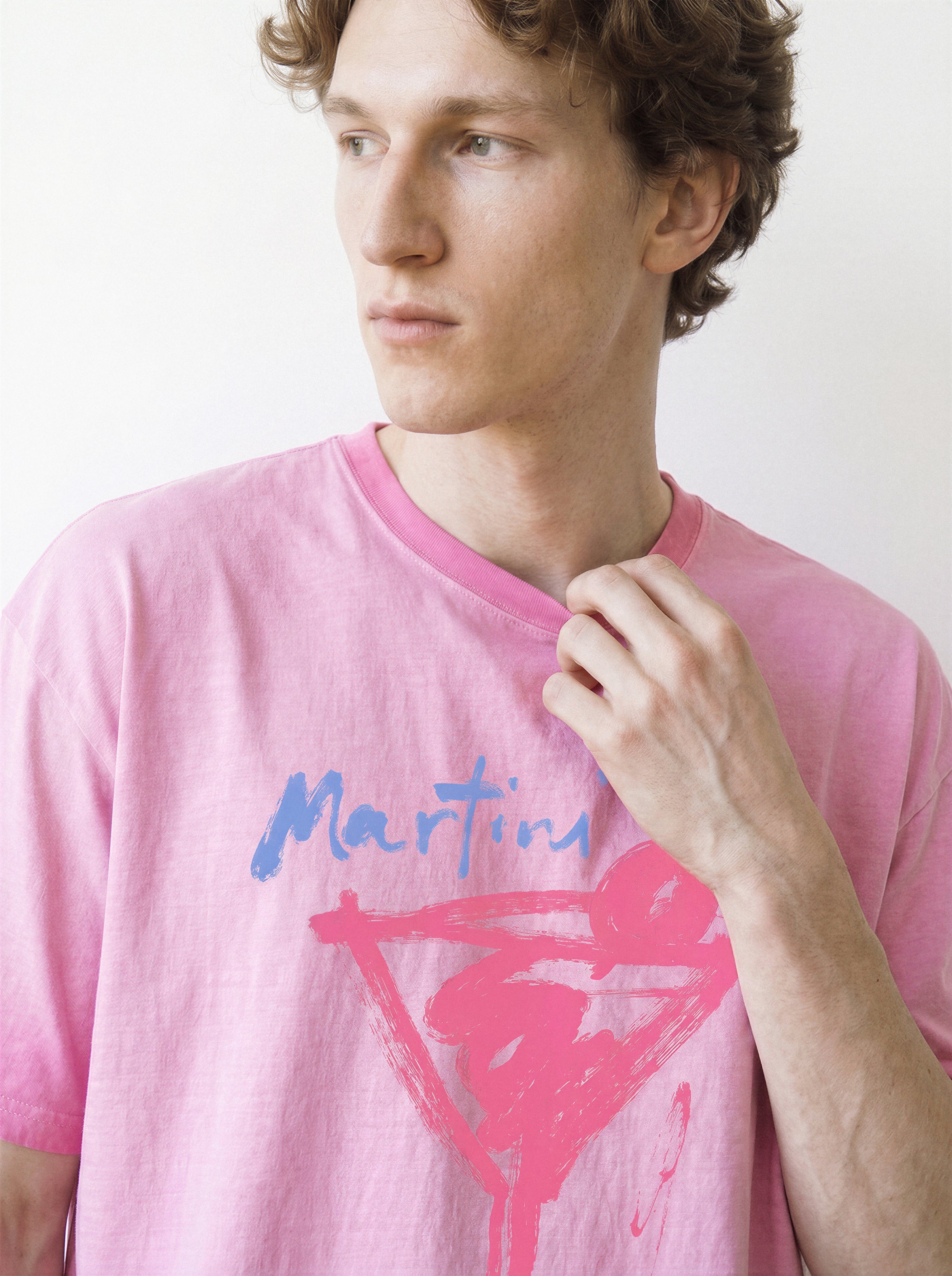 Close-up shot of a male model adjusting his collar and looking away, highlighting the 230g premium cotton fit of an aura pink tee with a casual ink stroke cocktail illustration.
