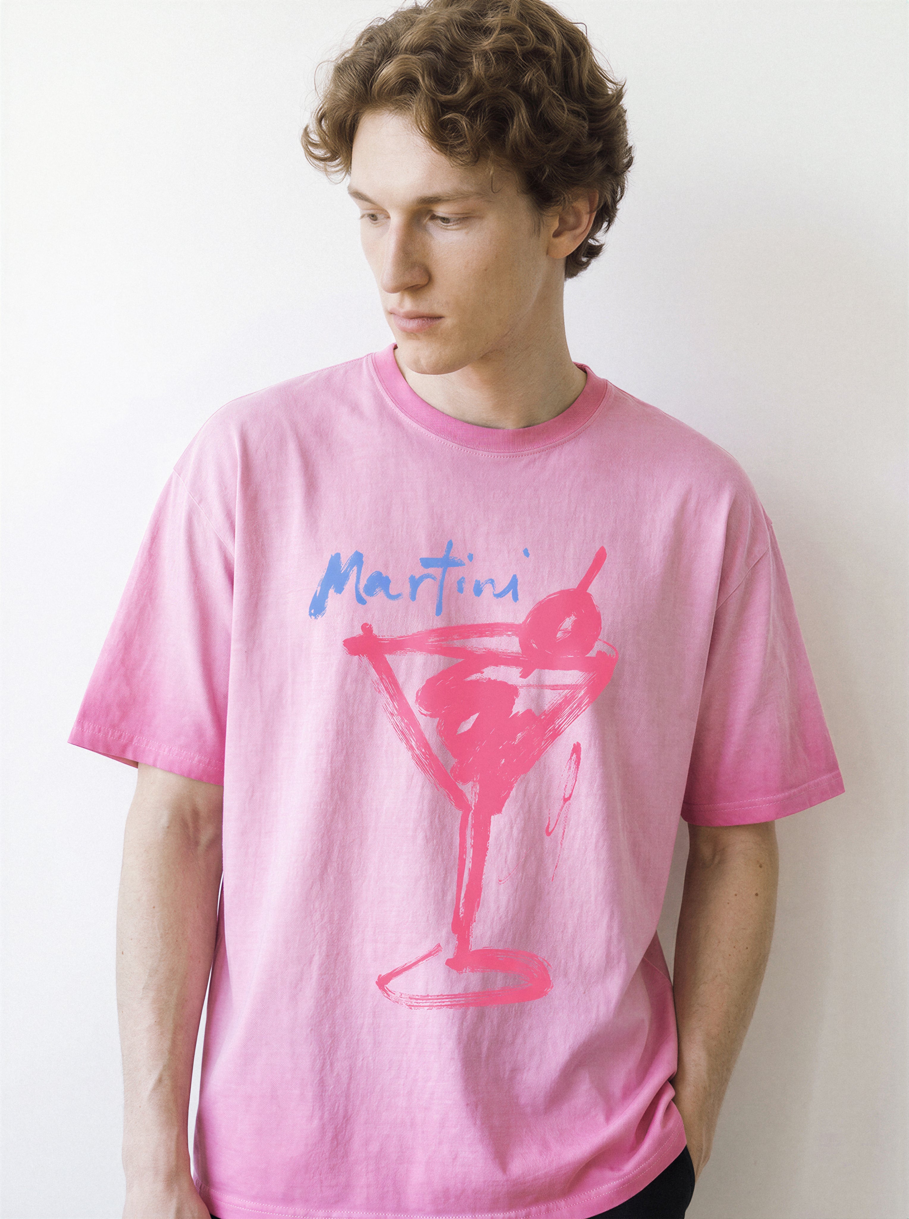 Front portrait of a male model looking down, wearing an aura pink heavyweight boxy fit graphic tee featuring a bold raw ink stroke martini glass sketch.