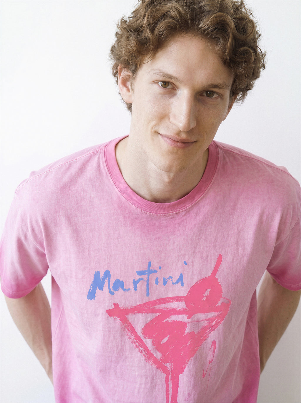 Front view of a male model smiling at the camera, demonstrating the relaxed drape of an aura pink structured streetwear t-shirt with a raw ink martini glass design.