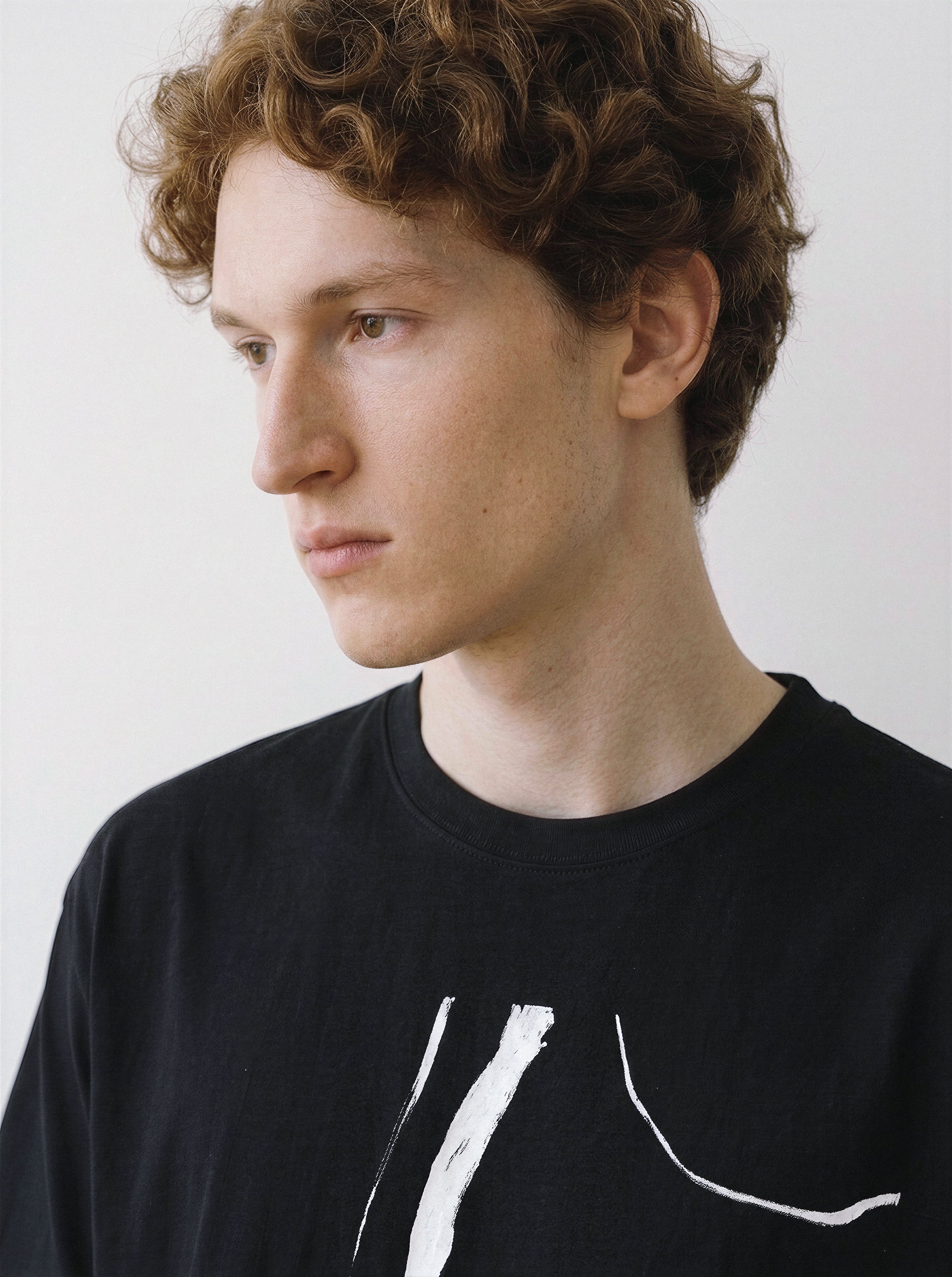 Close-up shot of a male model looking away, emphasizing the raw abstract brush strokes of the wild horses graphic on a black oversized tee.