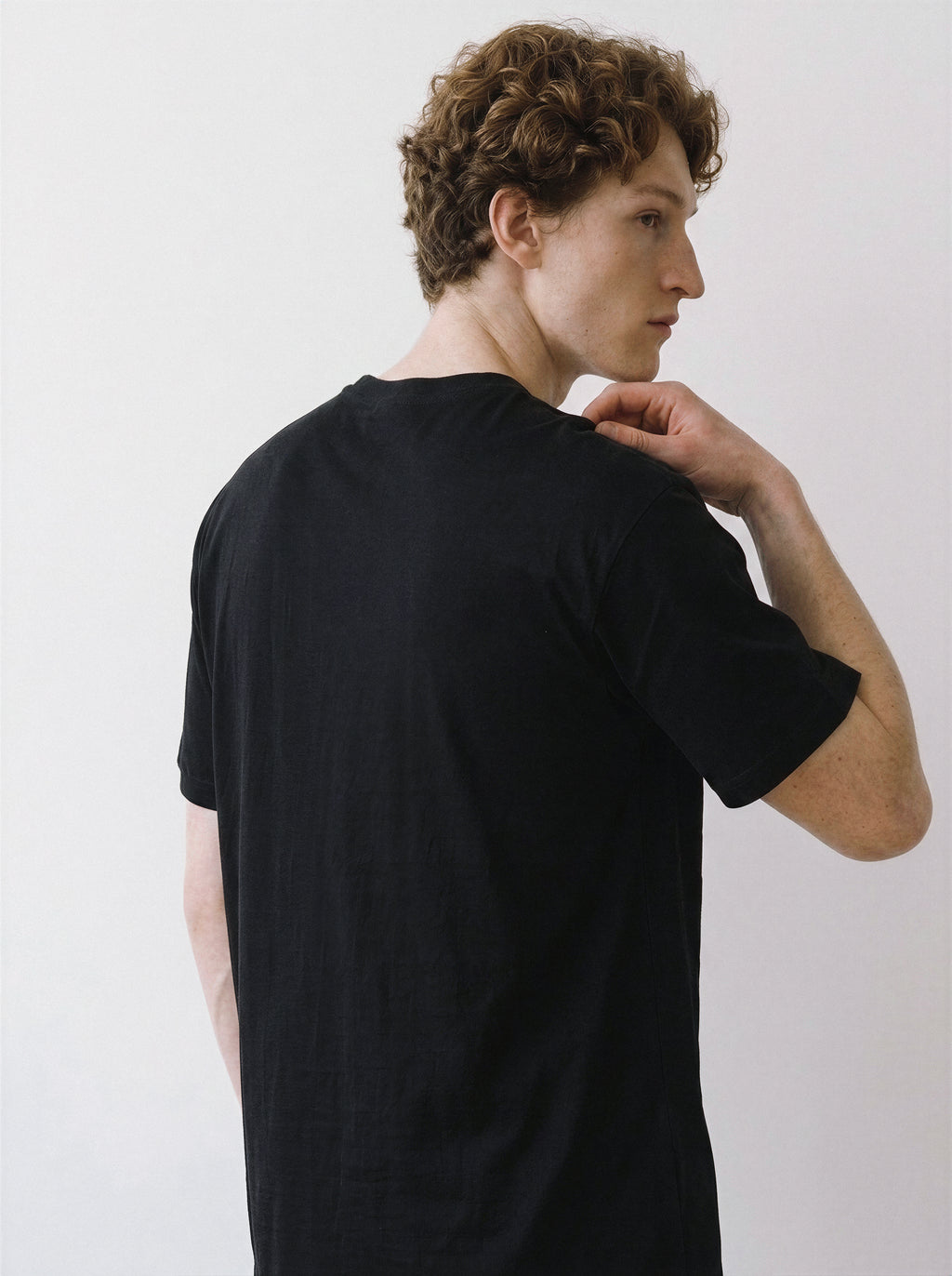 Back and side angle view of a male model looking over his shoulder, showcasing the comfortable fit of a black oversized t-shirt.