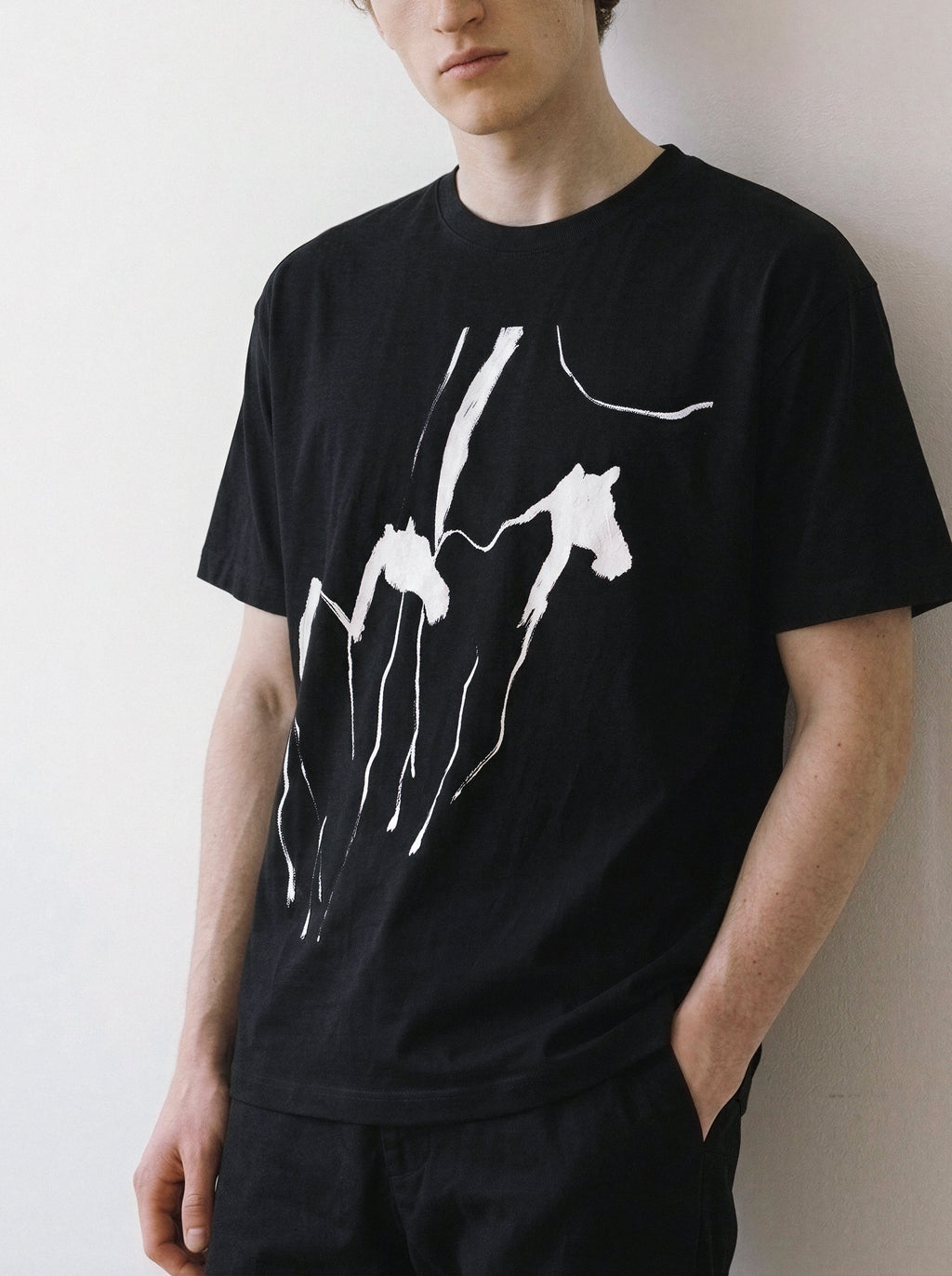 Angled view of a male model standing in a relaxed posture, wearing a black oversized graphic tee featuring an explosive energy running horses abstract print.