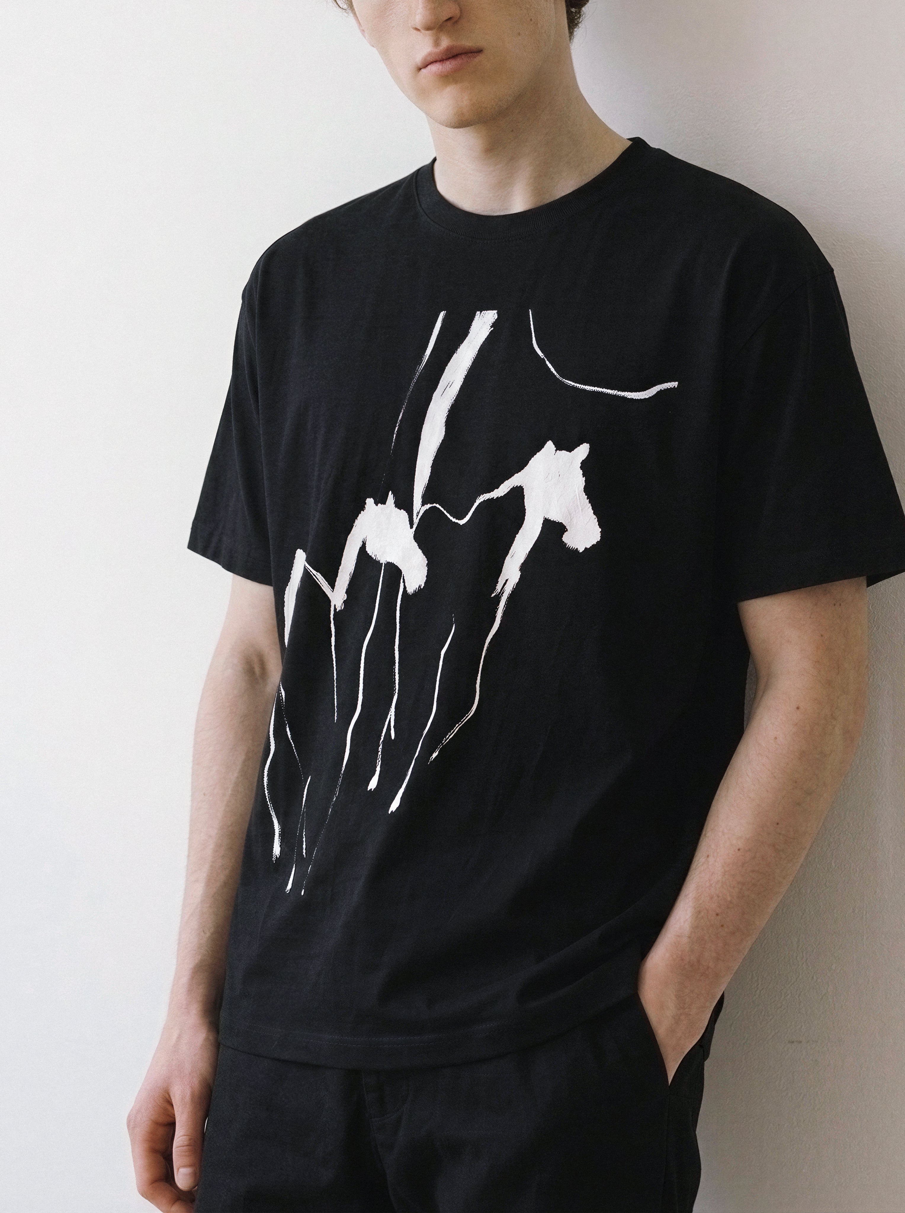 Angled view of a male model standing in a relaxed posture, wearing a black oversized graphic tee featuring an explosive energy running horses abstract print.