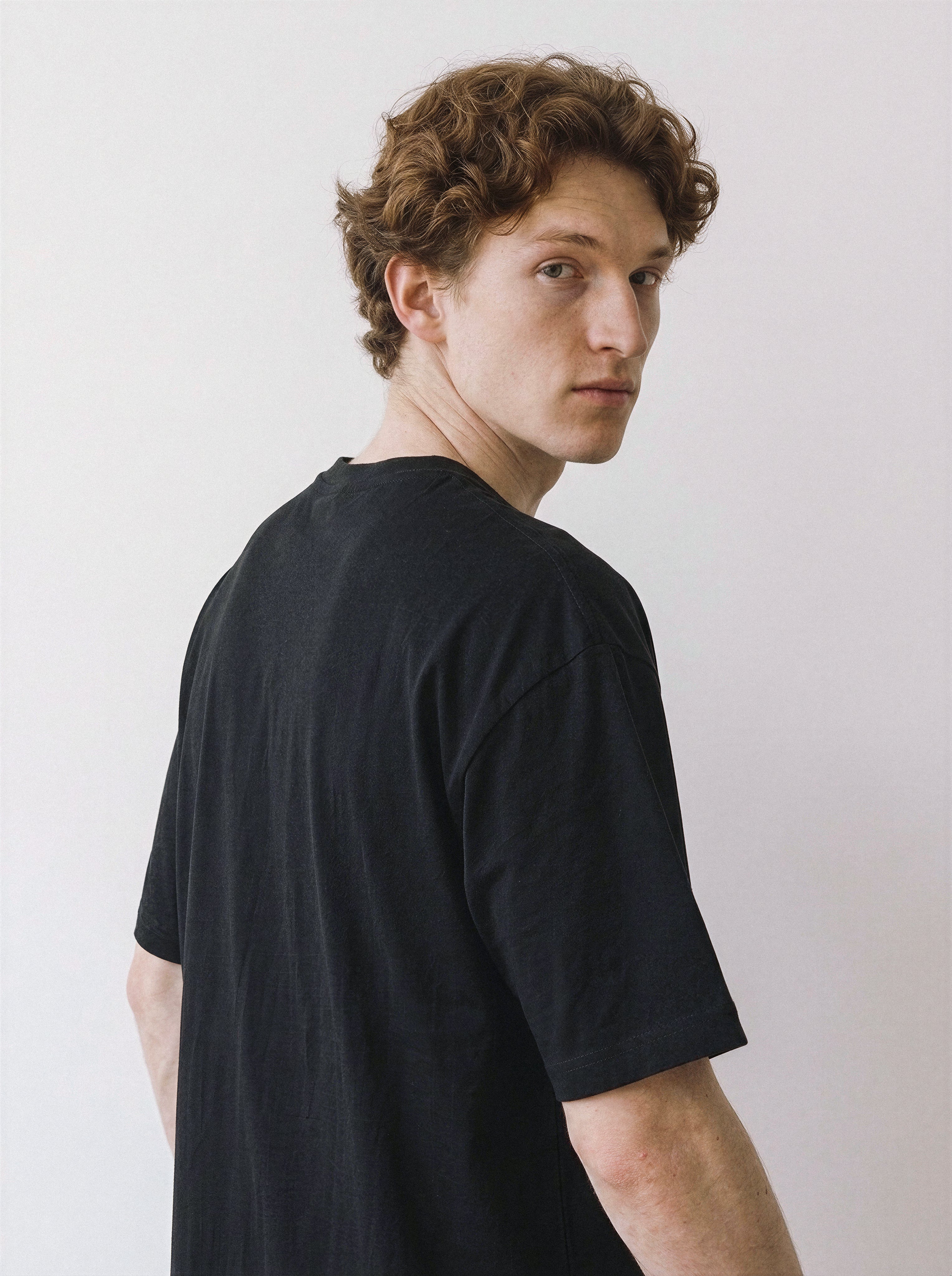 Side and back profile of a model looking over his shoulder, wearing a black oversized t-shirt emphasizing the relaxed fit and feline line art aesthetic.