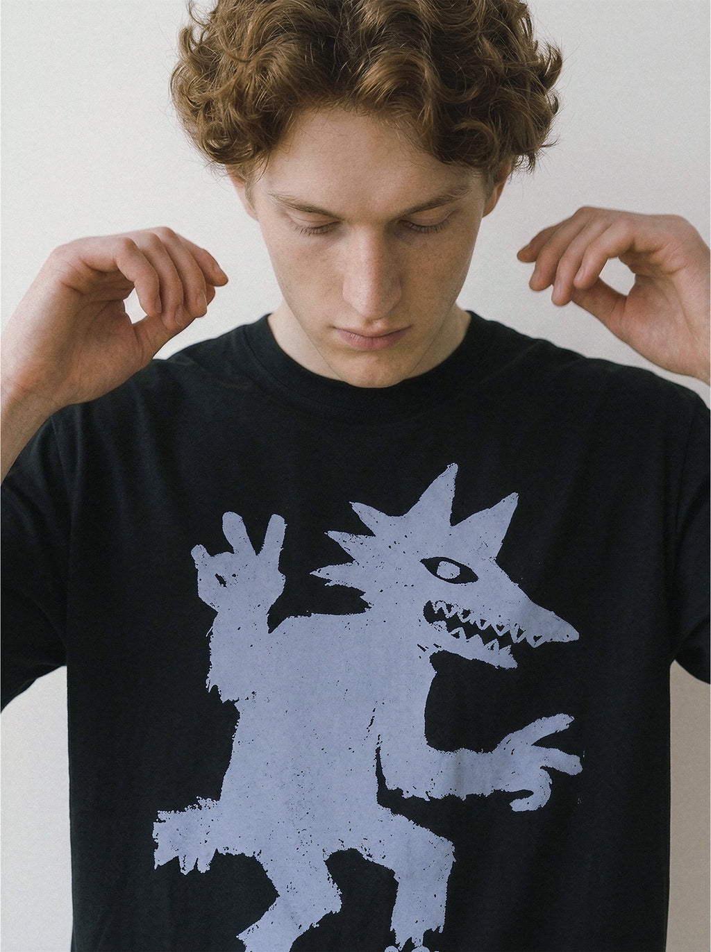 A male model looking down and adjusting the collar of a black oversized streetwear t-shirt with a quirky sneaker-wearing monster graphic.