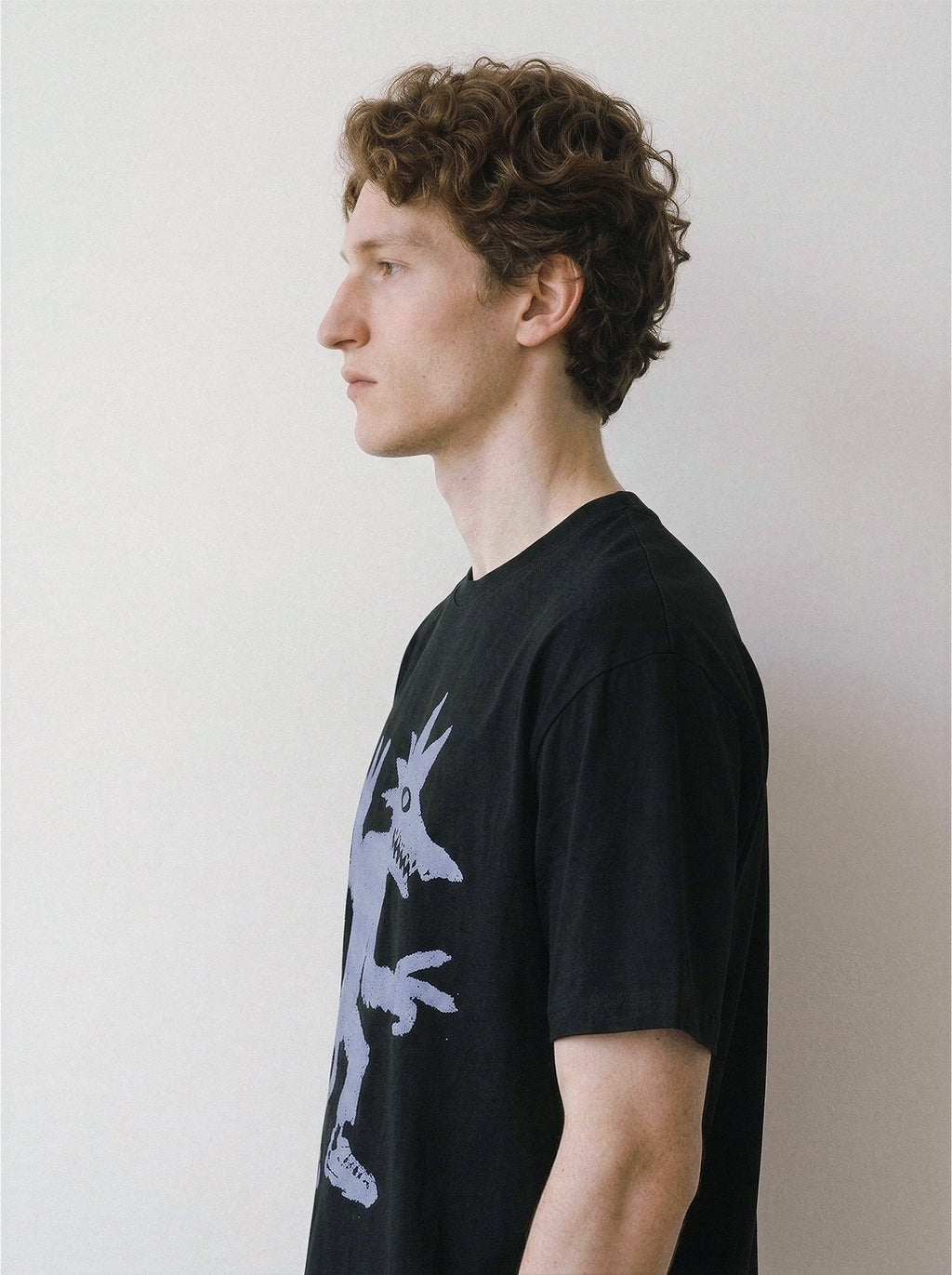 Side profile of a model wearing a black 180g premium cotton tee highlighting an edgy street-smart monster doodle design.