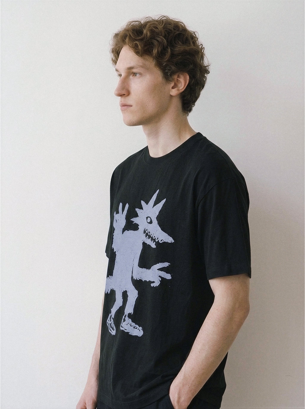 Three-quarter view of a male model wearing a black oversized t-shirt featuring an edgy skate-culture peace sign monster doodle print.