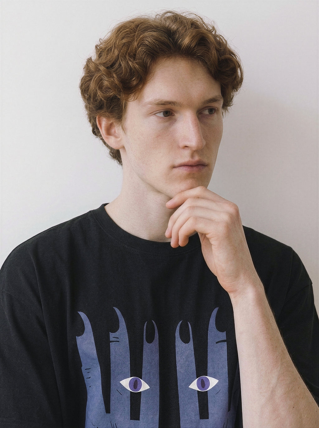 Portrait of a male model resting his hand on his chin and looking to the right, wearing a black premium cotton tee with a striking surreal hands graphic.