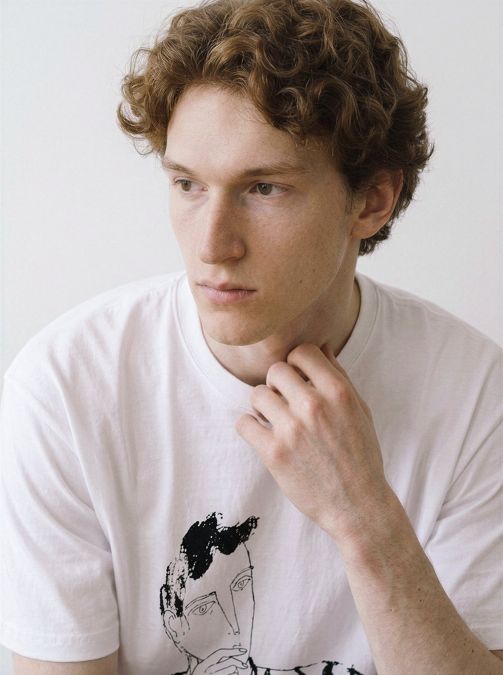 A close-up of a male model posing in a white blank stare portrait line art graphic tee, capturing the distinctive raw sketch graphic detail.