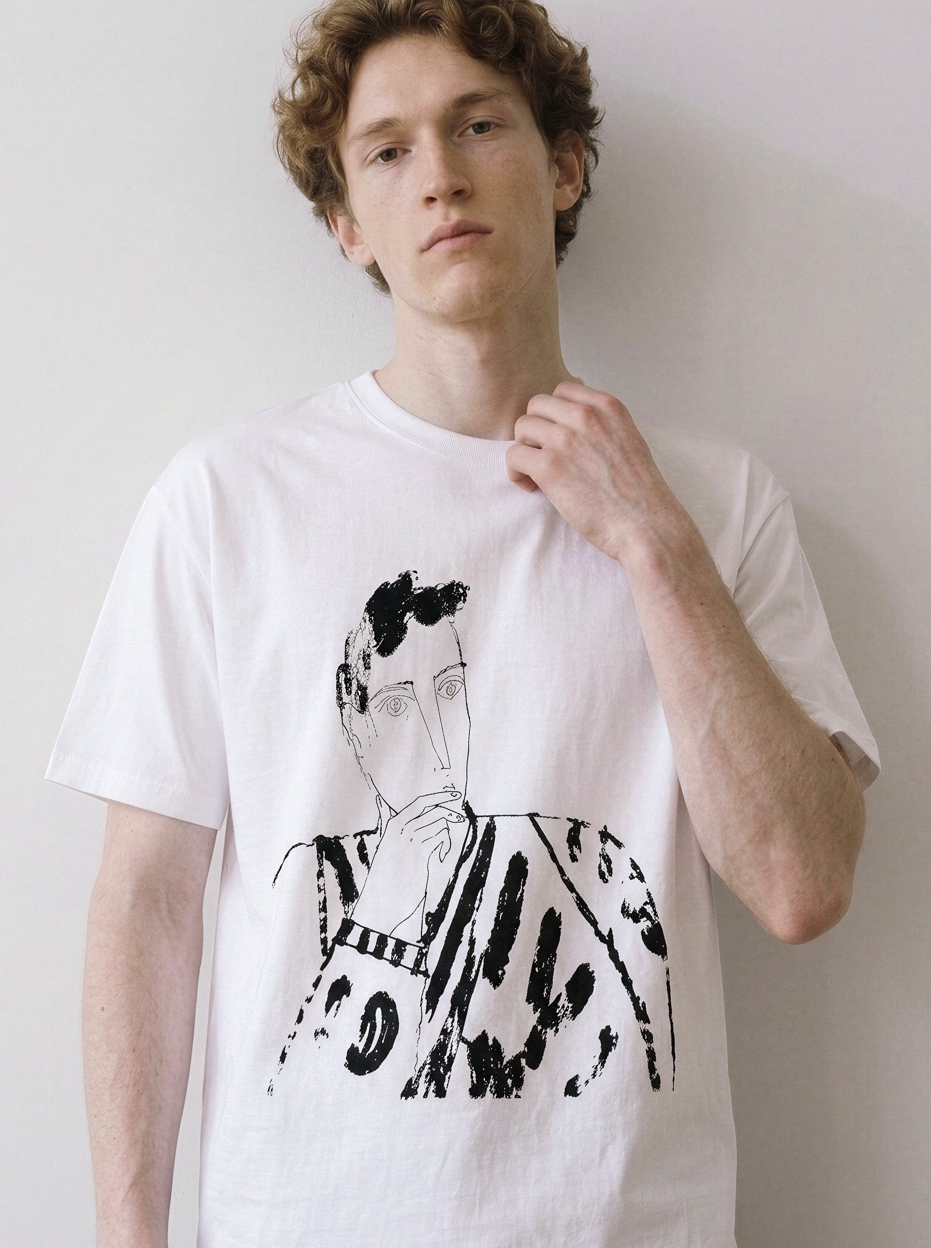 A male model leaning against a wall wearing a white blank stare portrait line art graphic tee, showcasing the heavy stroke sketch and relaxed unisex fit.