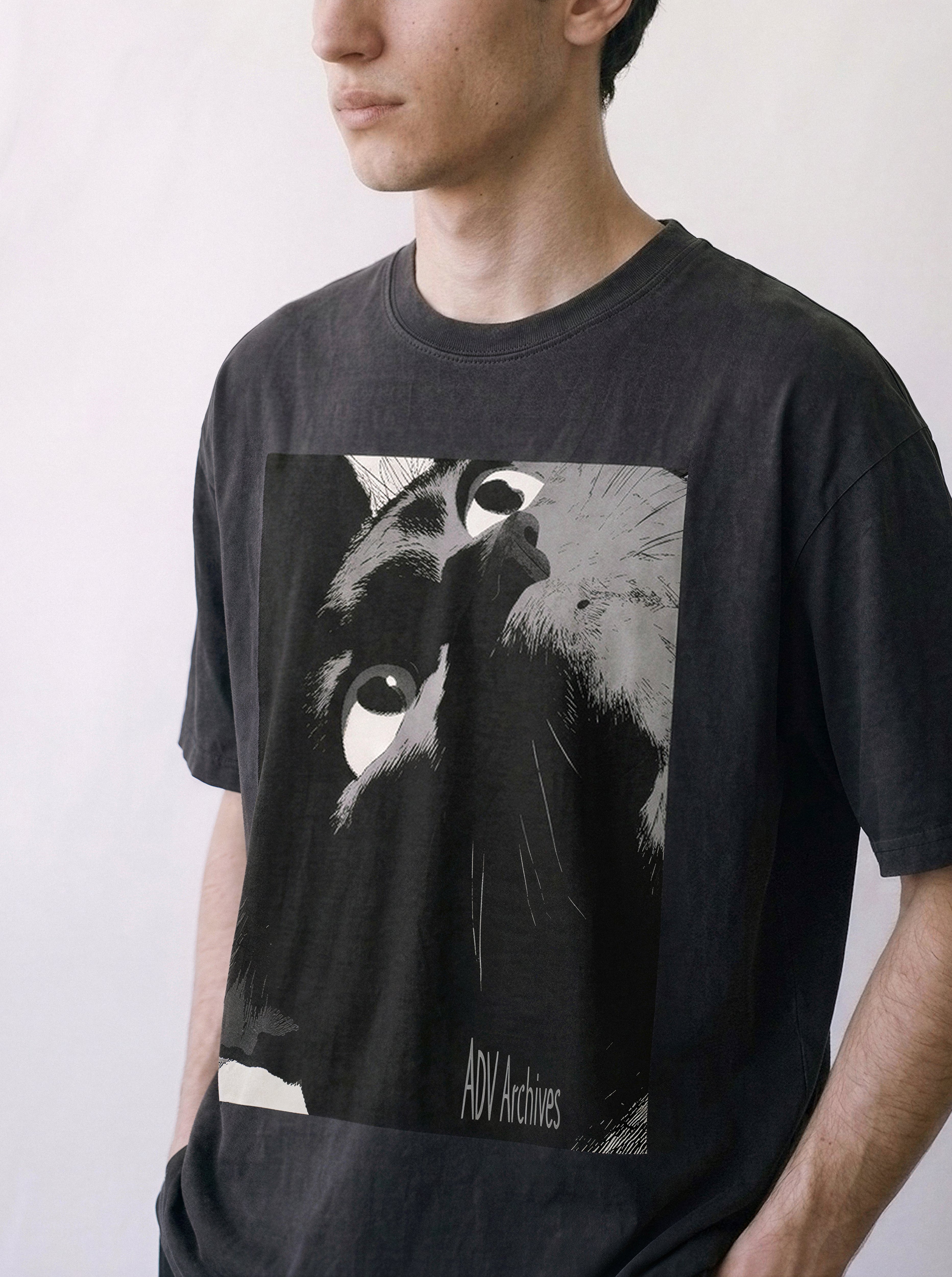 A half-body shot of a male model looking away wearing a black cat gaze manga panel graphic tee, displaying the bold line art streetwear style.