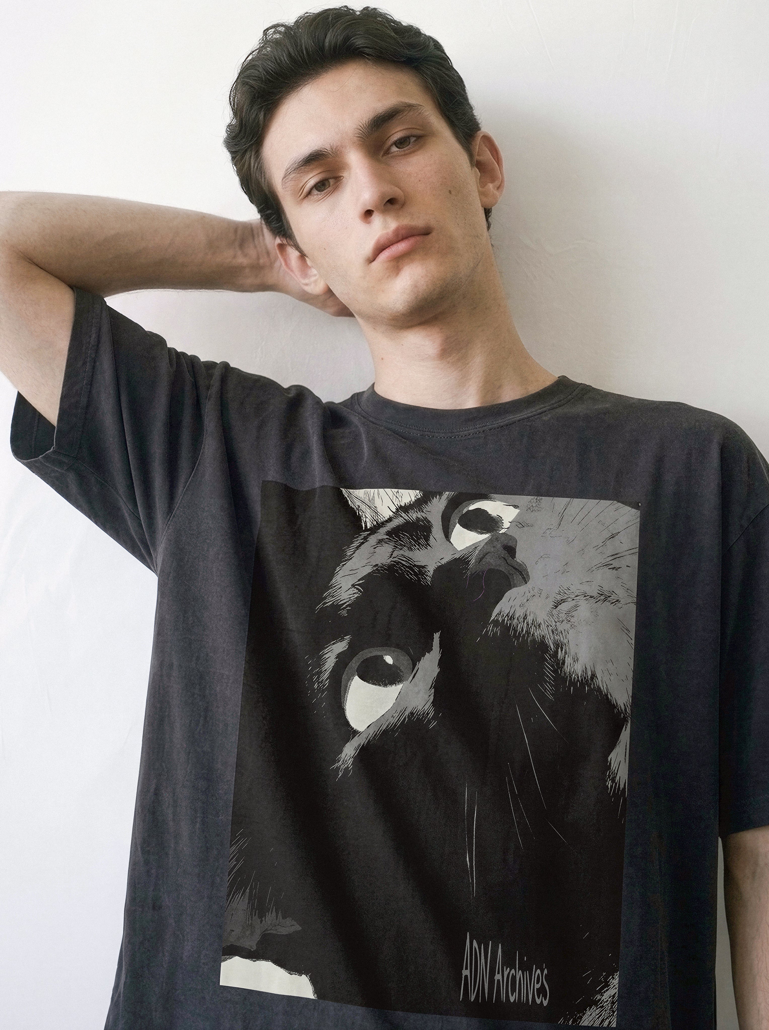 A male model with his hand behind his neck wearing a black cat gaze manga panel graphic tee, showcasing the high-contrast feline ink close-up and minimalist streetwear vibe.
