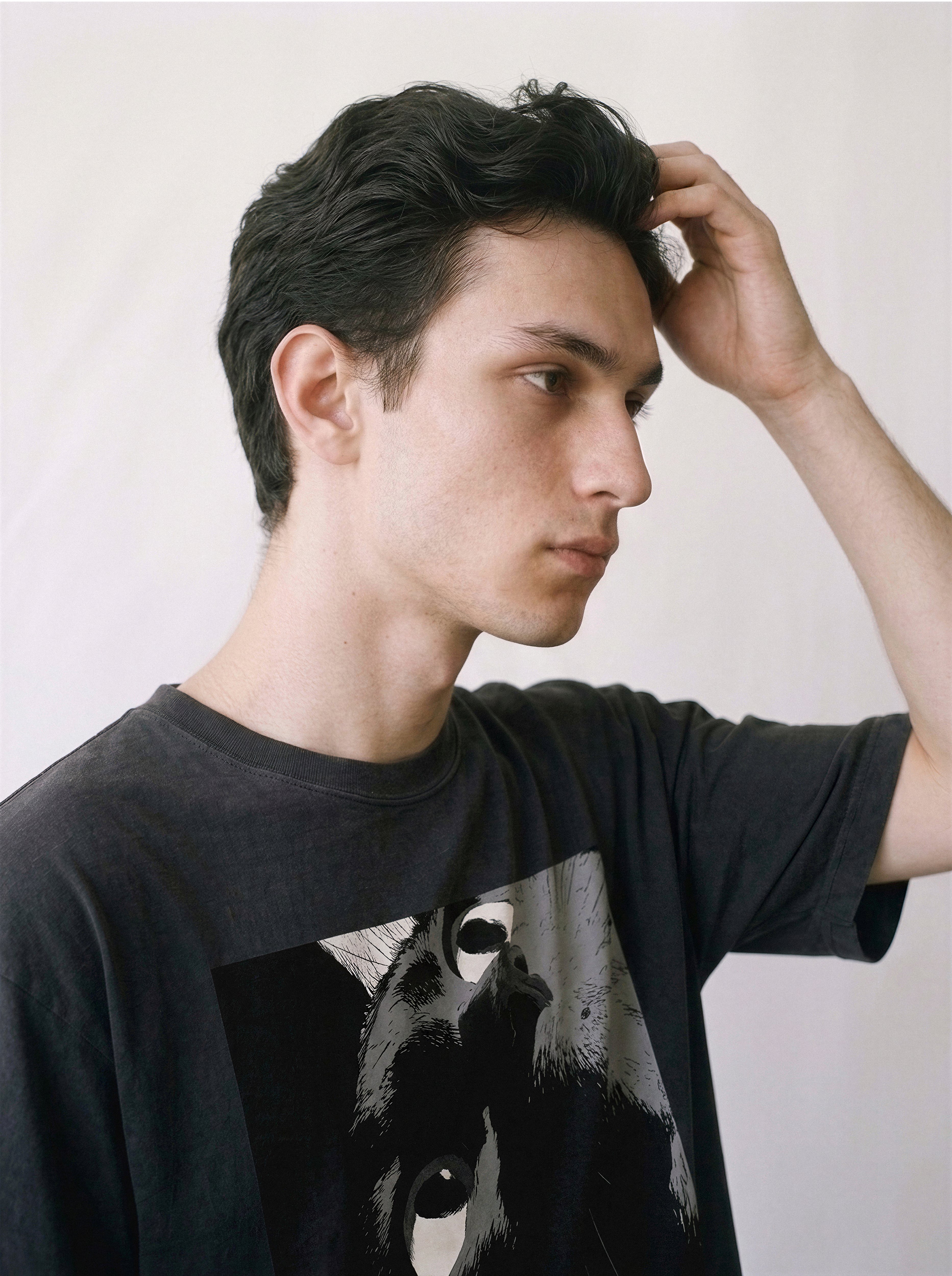 A side profile of a male model with his hand in his hair wearing a black cat gaze manga panel graphic tee, showcasing the raw feline stare graphic.