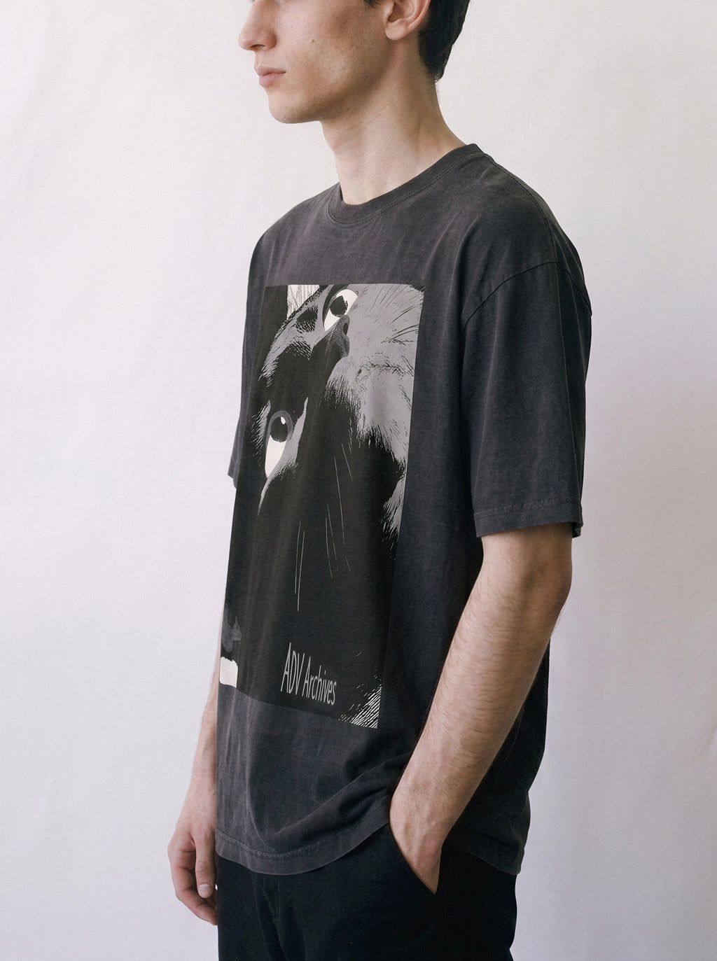 A side profile of a male model wearing a black cat gaze manga panel graphic tee, demonstrating the garment's drape and distinct independent manga graphic.