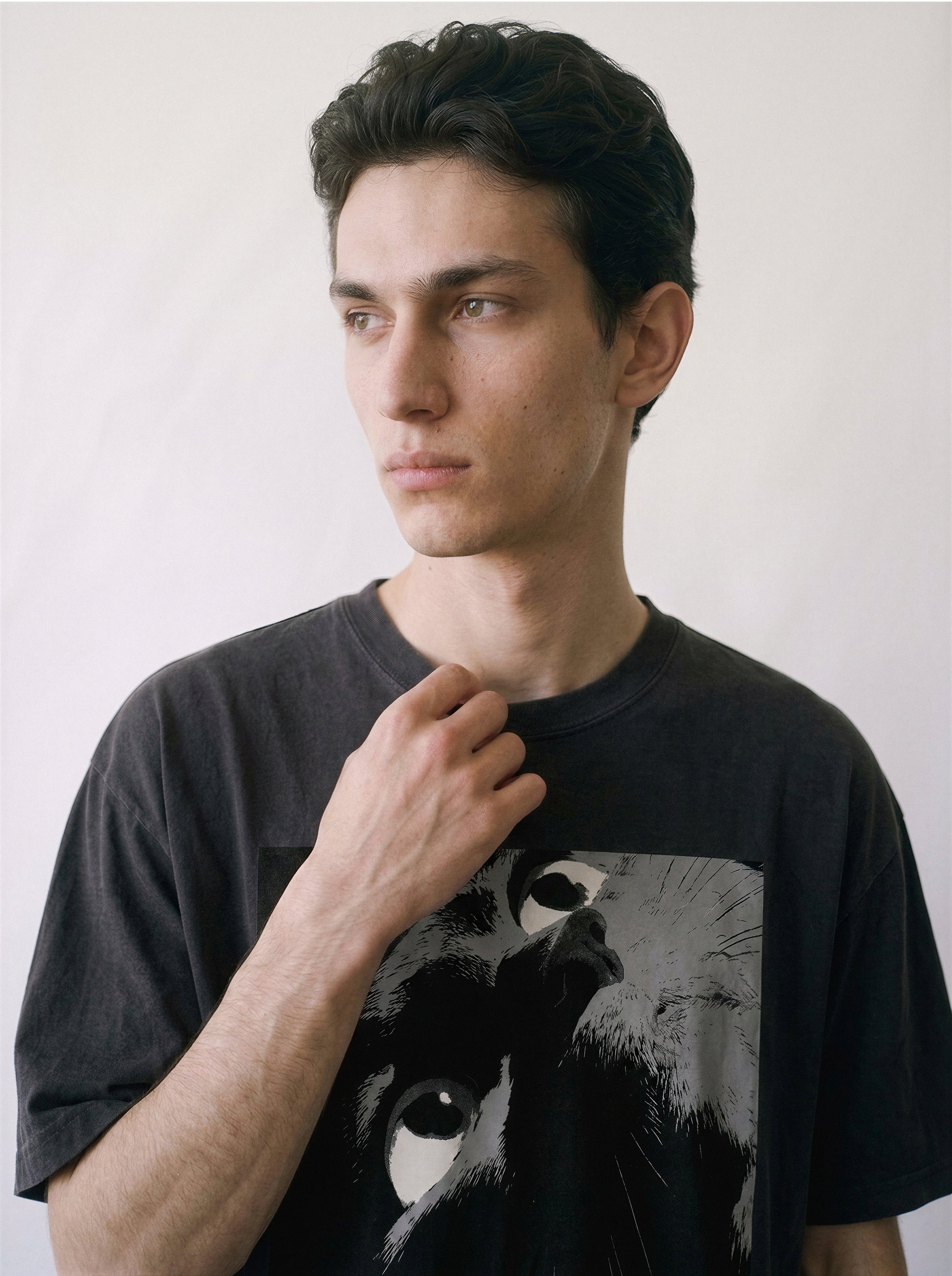 A male model touching his collar wearing a black cat gaze manga panel graphic tee, capturing the raw tension of the monochrome manga illustration.