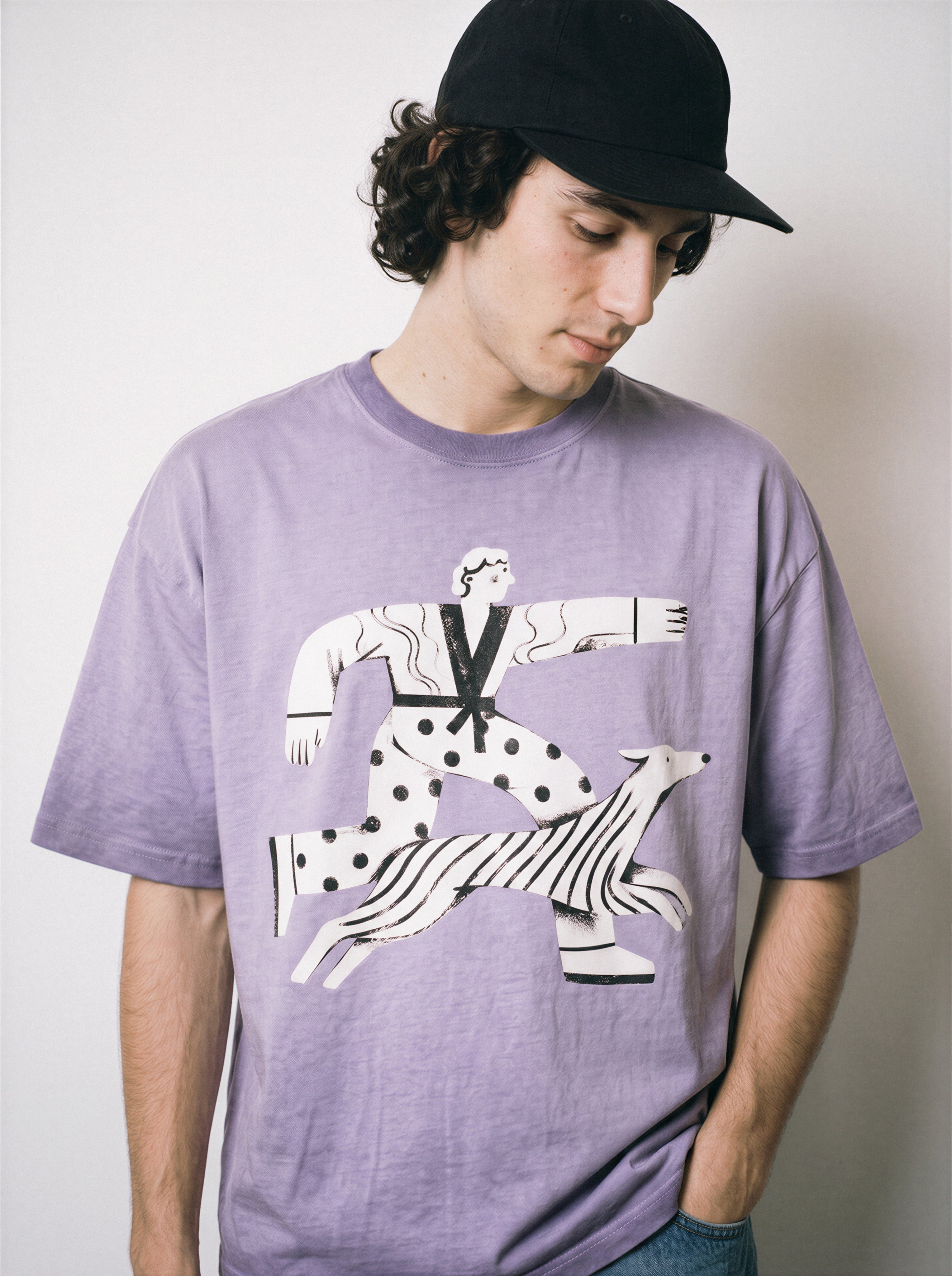 A male model looking down wearing an ombre violet confident stride boy and dog graphic tee, emphasizing the relaxed boxy fit and optimistic graphic design.