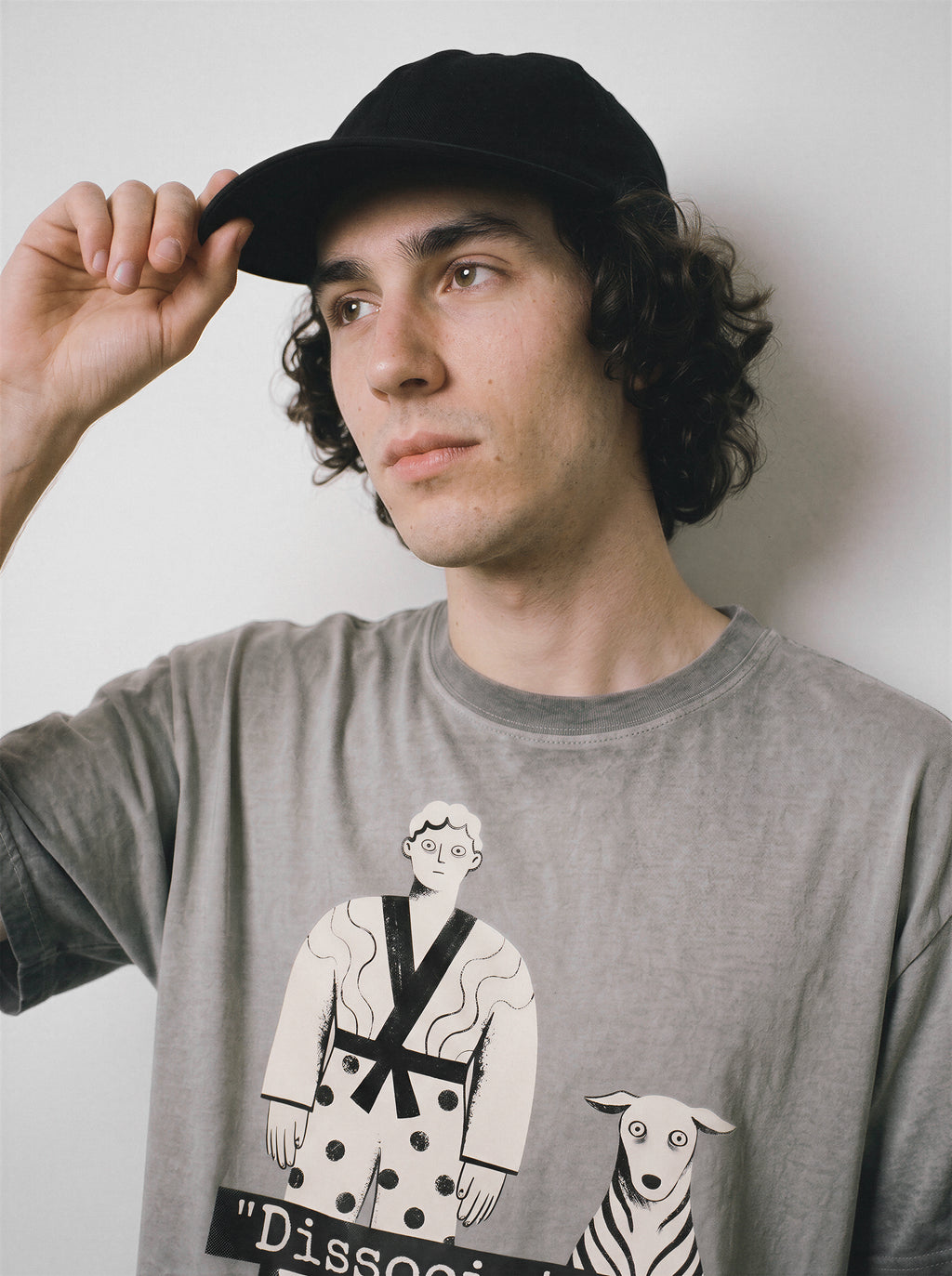 A male model adjusting his cap while looking away, wearing an ombre grey dissociating ironic graphic tee, highlighting the soul offline mood and dry humor apparel style.