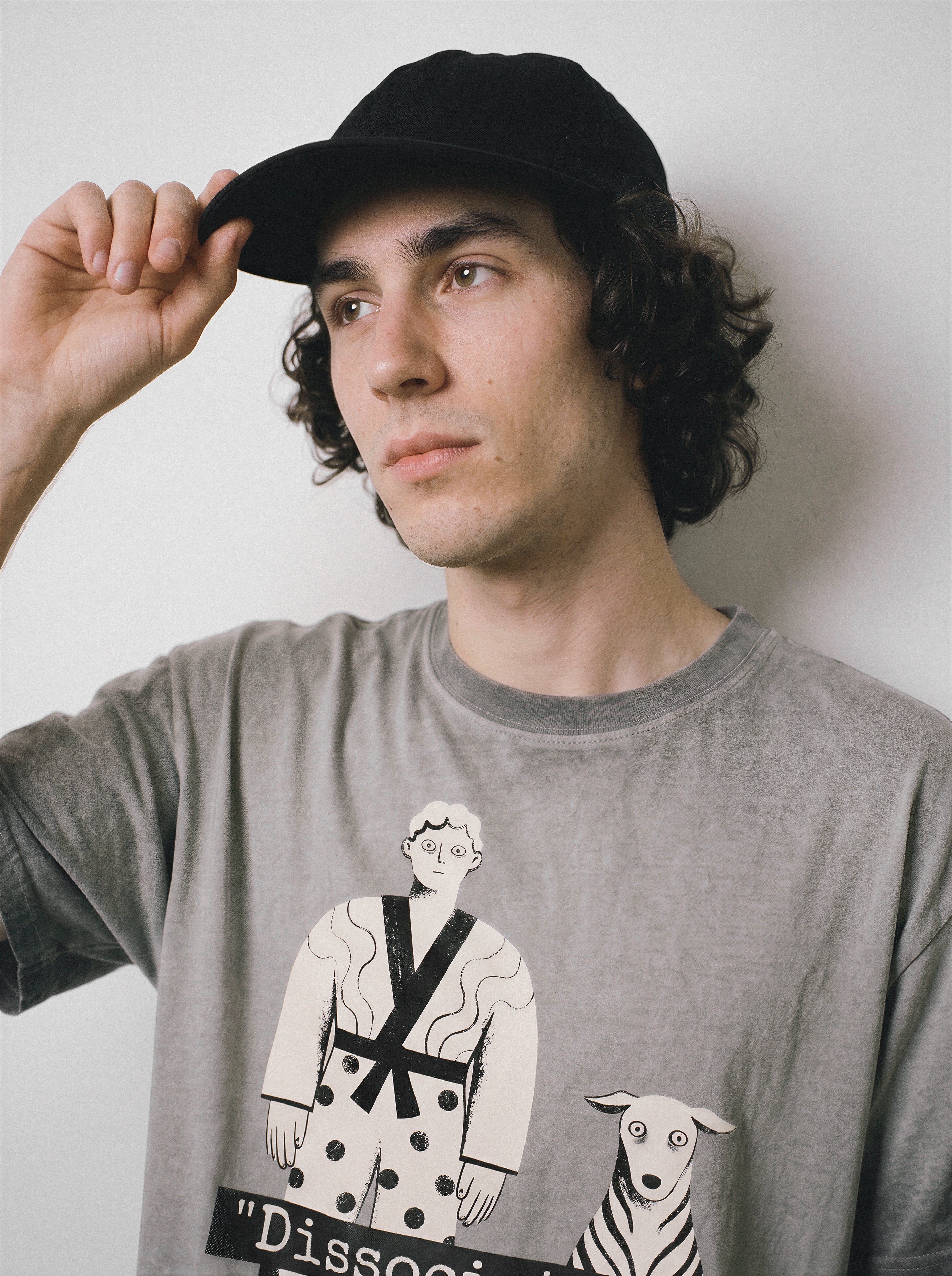 A male model adjusting his cap while looking away, wearing an ombre grey dissociating ironic graphic tee, highlighting the soul offline mood and dry humor apparel style.