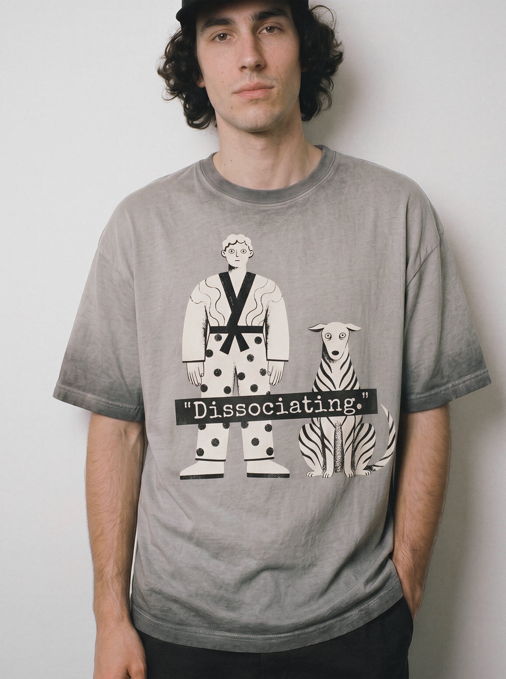 A front view of a male model with a deadpan expression wearing an ombre grey dissociating ironic graphic tee, showcasing the sarcastic boy and dog print and Gen Z existential streetwear vibe.