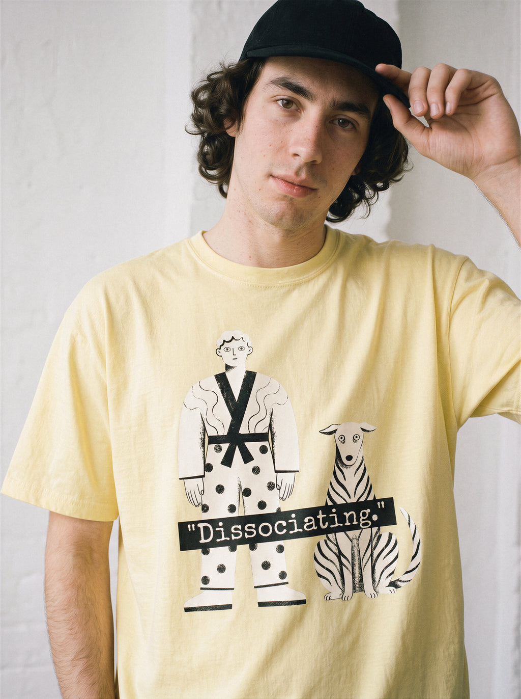 A male model adjusting his cap wearing a butter dissociating line art graphic tee, showcasing the immaculate posture print and soul offline aesthetic.
