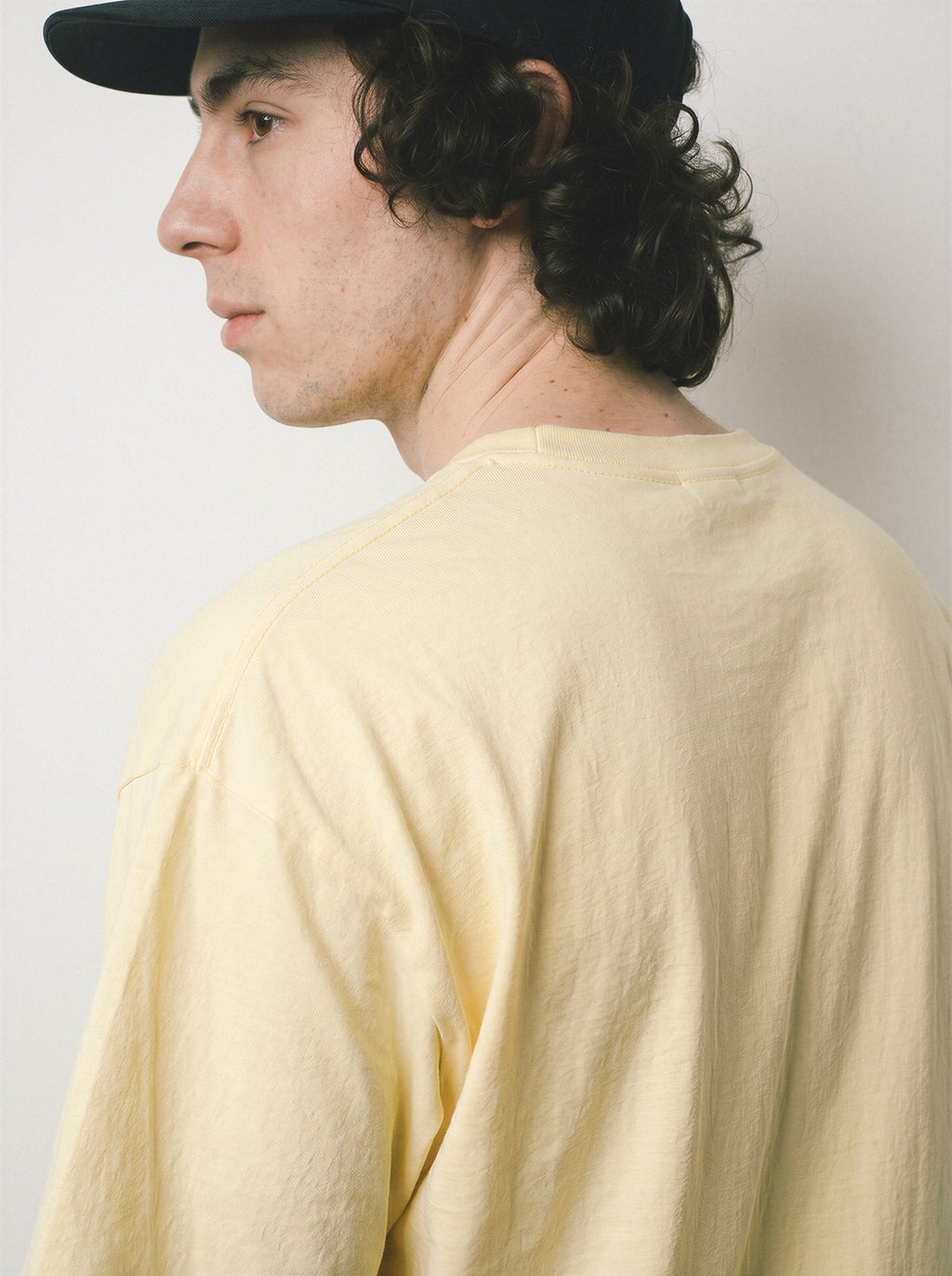 A back view of a male model looking over his shoulder wearing a butter dissociating line art graphic tee, capturing the casual drape and everyday minimalist streetwear vibe.