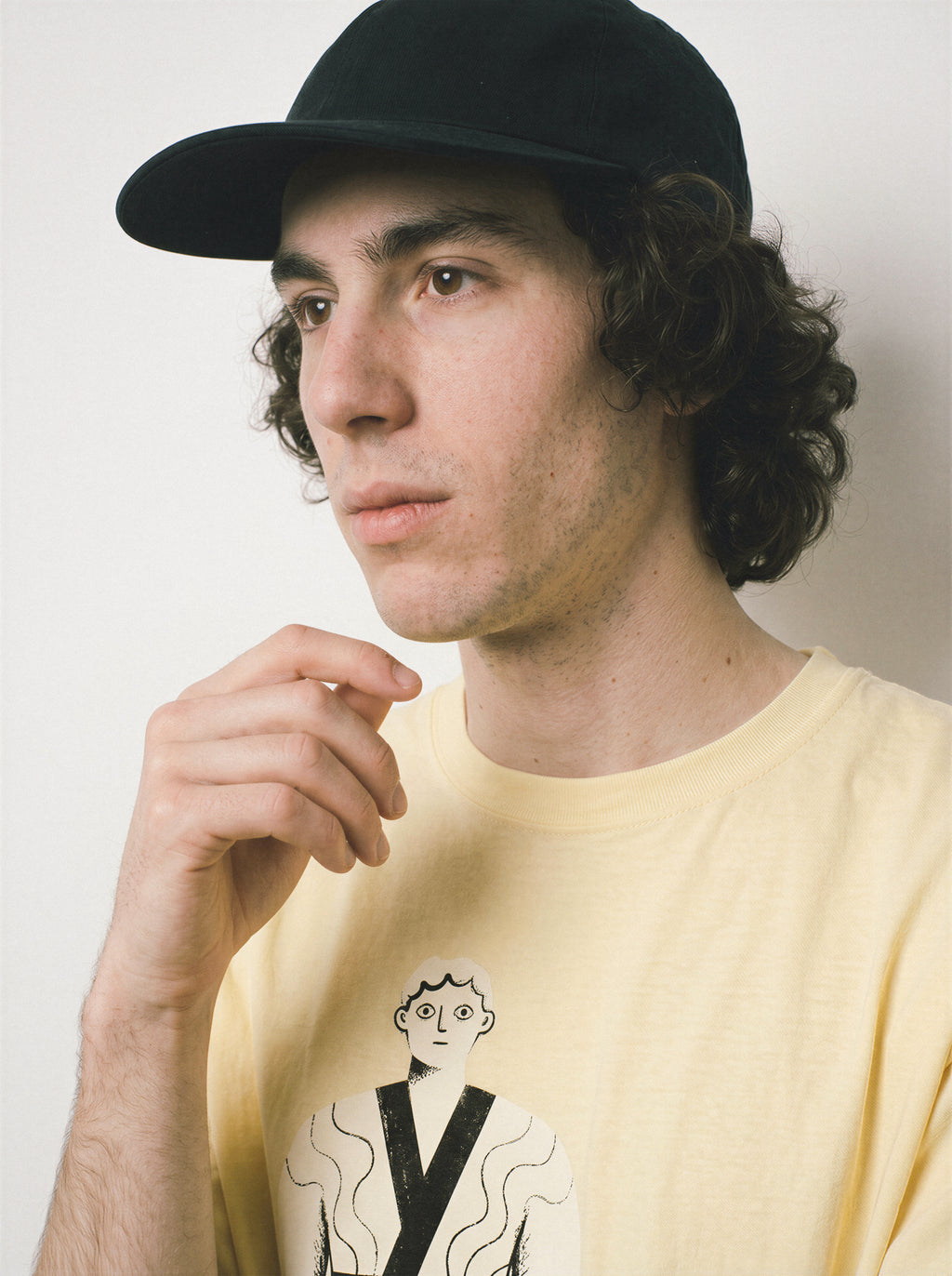 A close-up of a male model touching his chin wearing a butter dissociating line art graphic tee, focusing on the deadpan illustration and pure line art graphic details.
