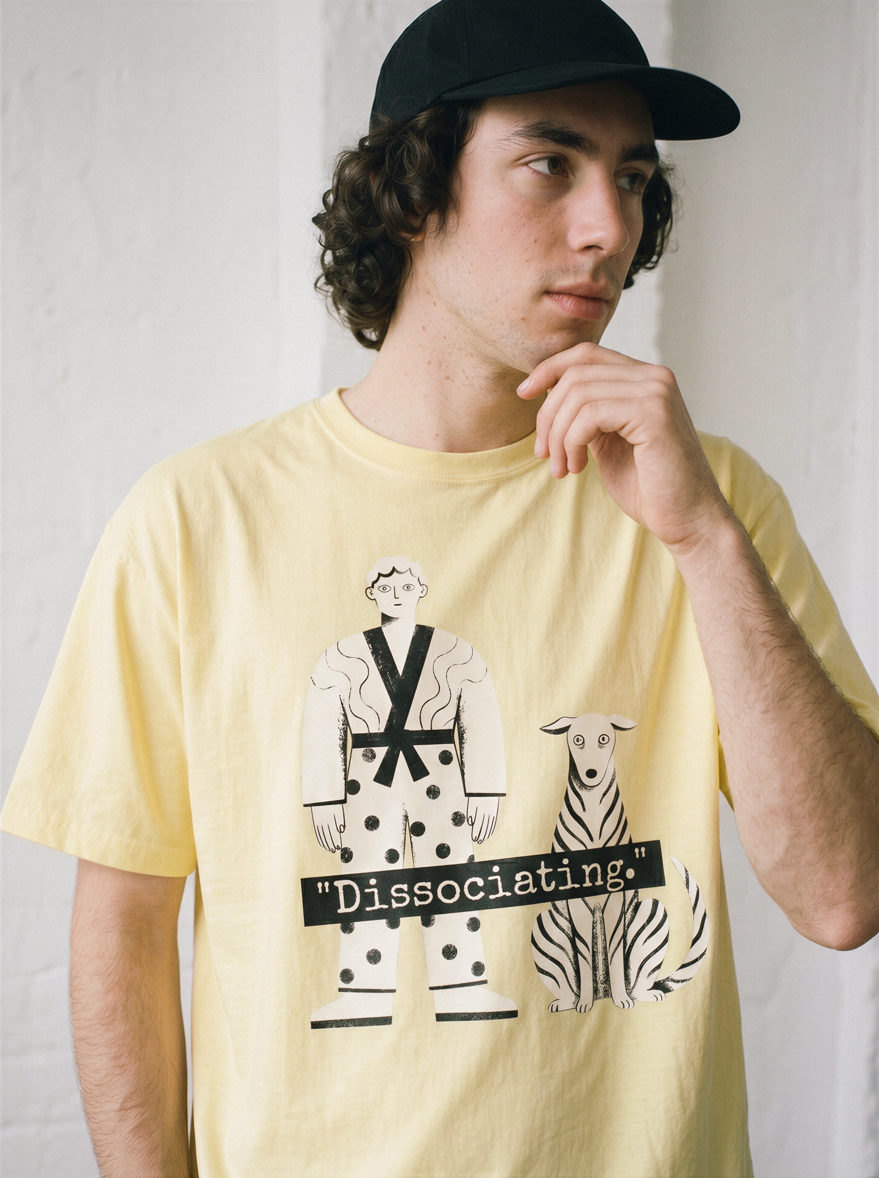 A male model touching his chin and looking down wearing a butter dissociating line art graphic tee, highlighting the pure line art form and detached state of mind.