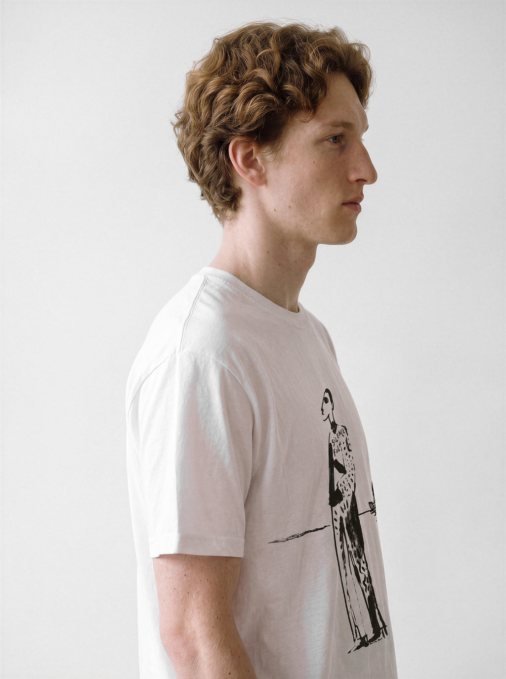 A side profile of a male model wearing a white mysterious elongated figure line art graphic tee, showcasing the hand-drawn ink illustration and relaxed unisex fit.