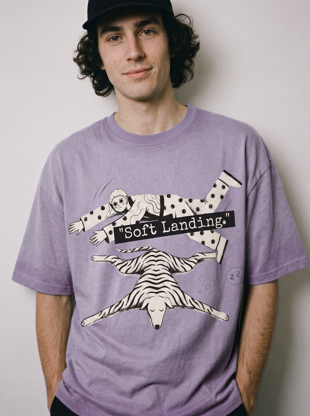 A male model with hands in his pockets wearing an ombre violet face down soft landing graphic tee, showcasing the existential streetwear vibe and lying flat print.