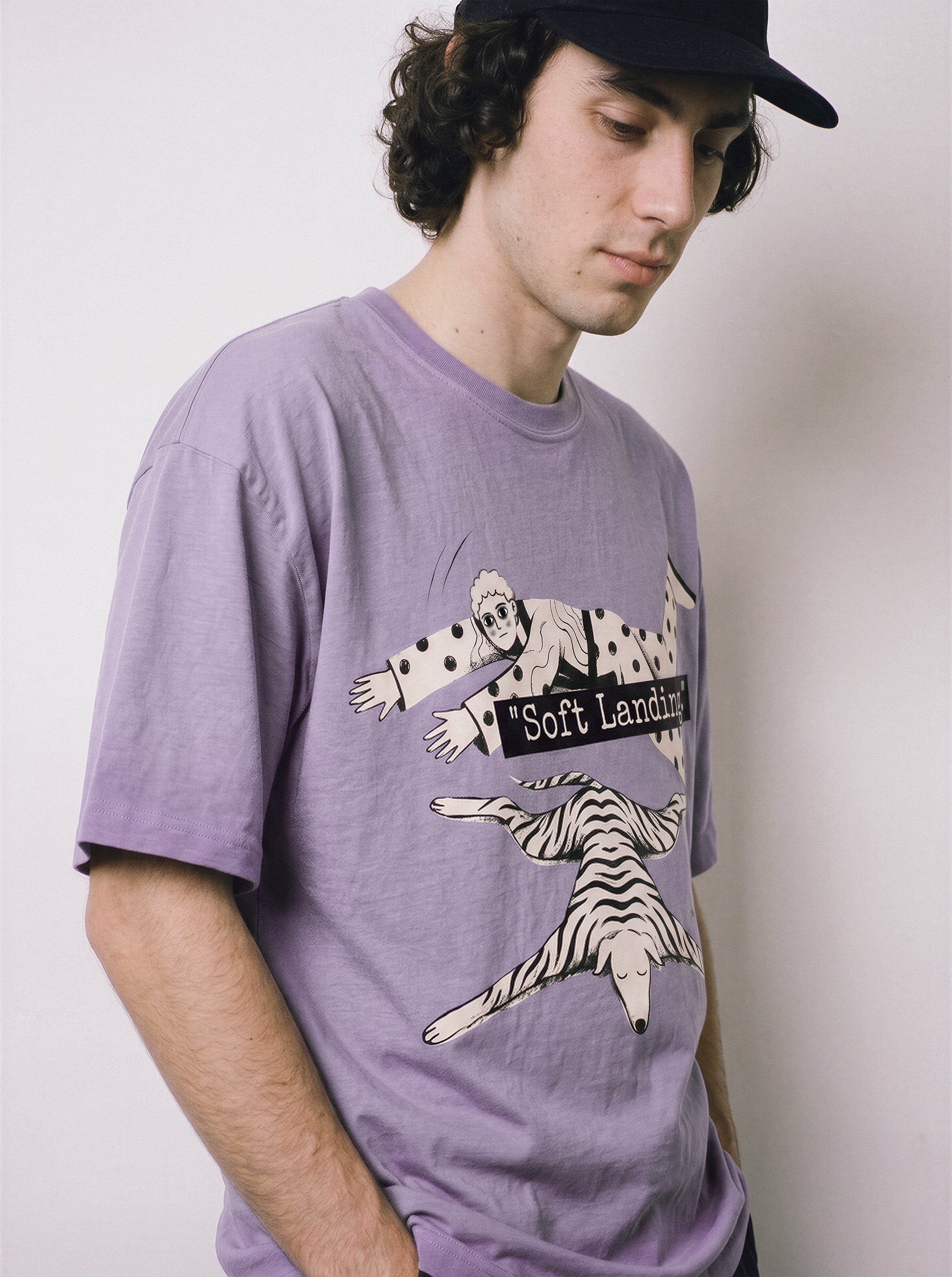A male model looking down and aside wearing an ombre violet face down soft landing graphic tee, emphasizing the relaxed boxy fit and economic miracle theme.