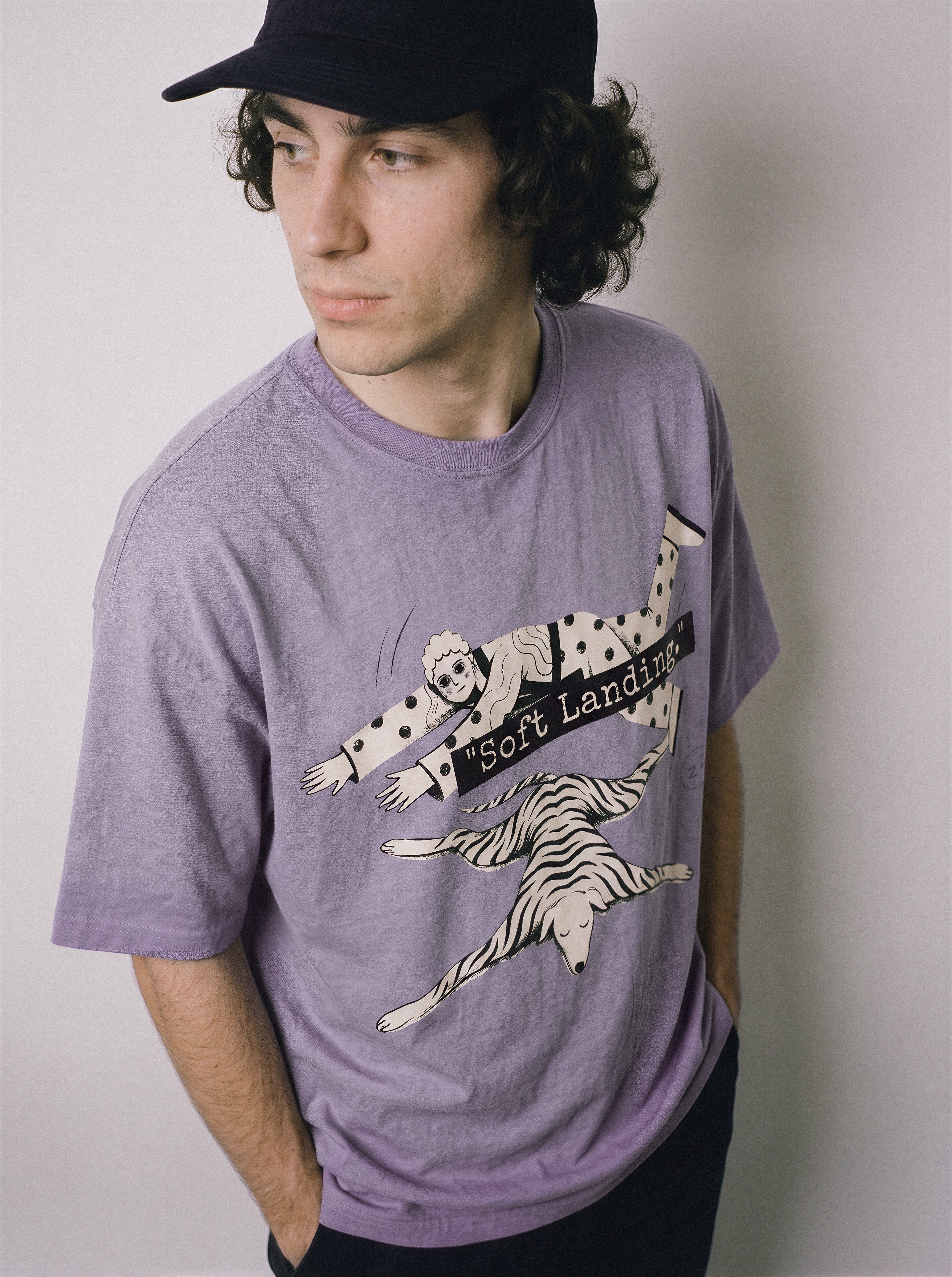 A male model looking over his shoulder wearing an ombre violet face down soft landing graphic tee, capturing the minimalist apparel style and face down boy and dog design.