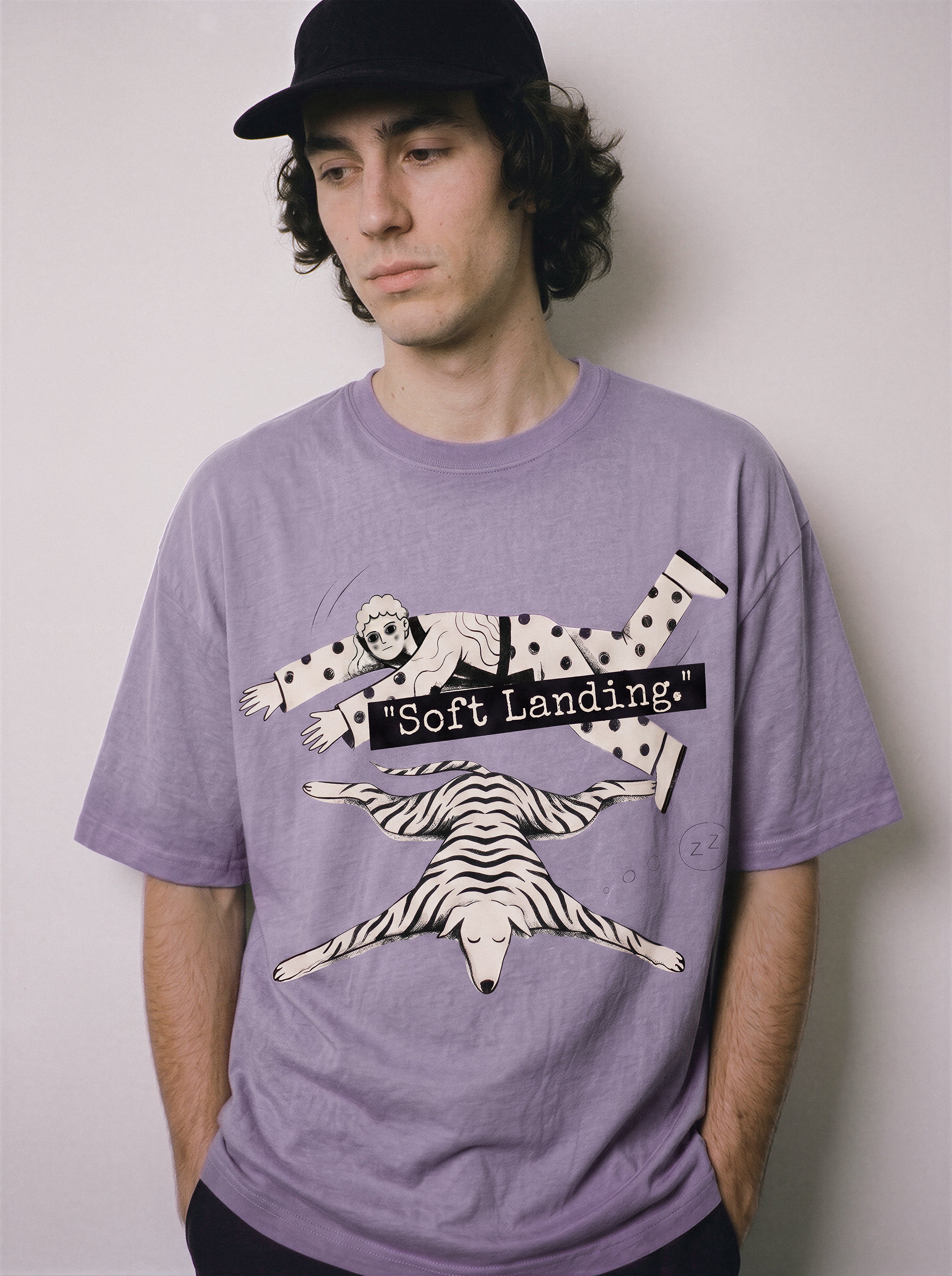 A male model looking straight down wearing an ombre violet face down soft landing graphic tee, displaying the casual drape and corporate dystopia vibe.