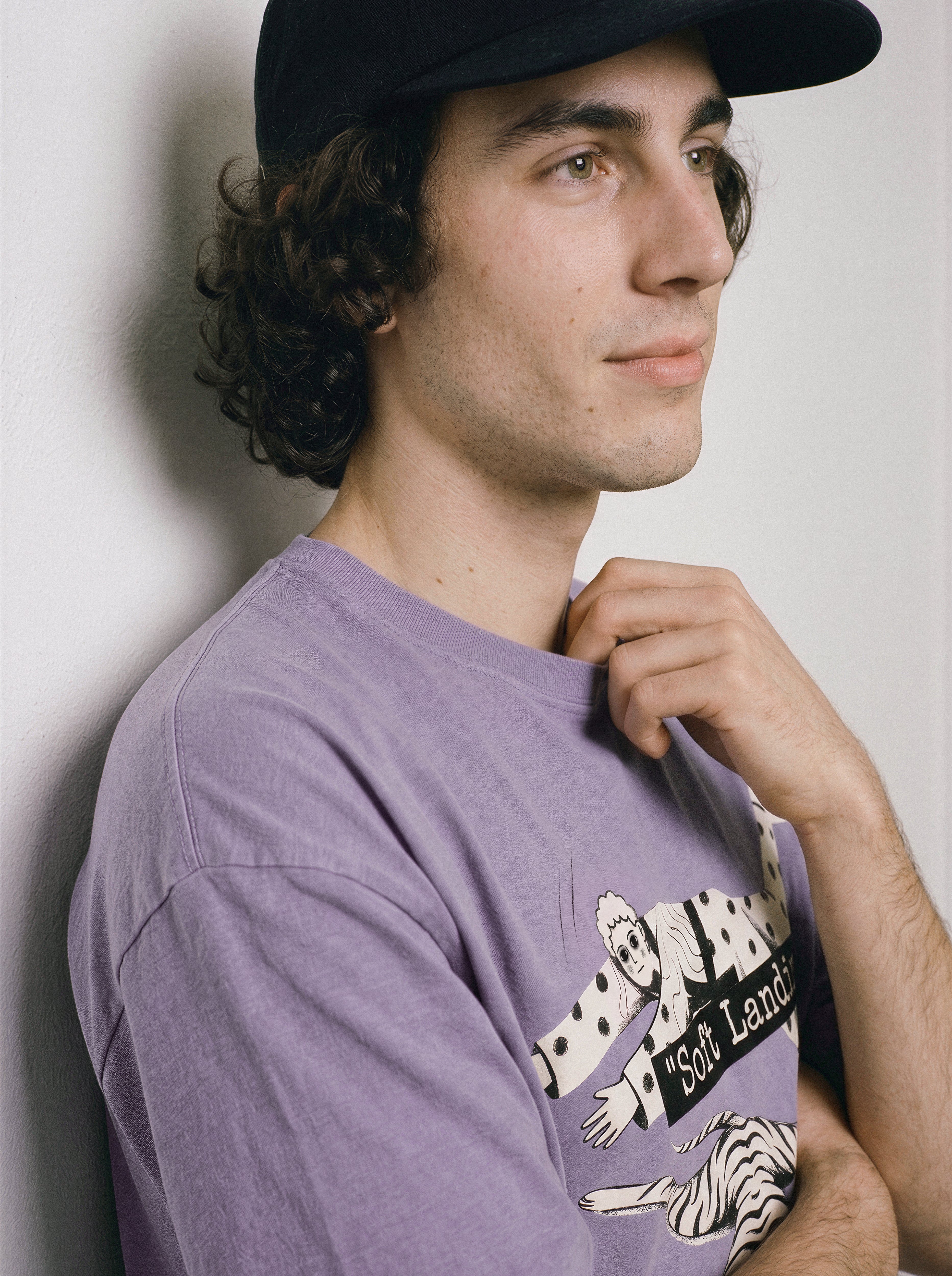 A side profile of a male model wearing an ombre violet face down soft landing graphic tee, featuring the deadpan lying flat illustration.