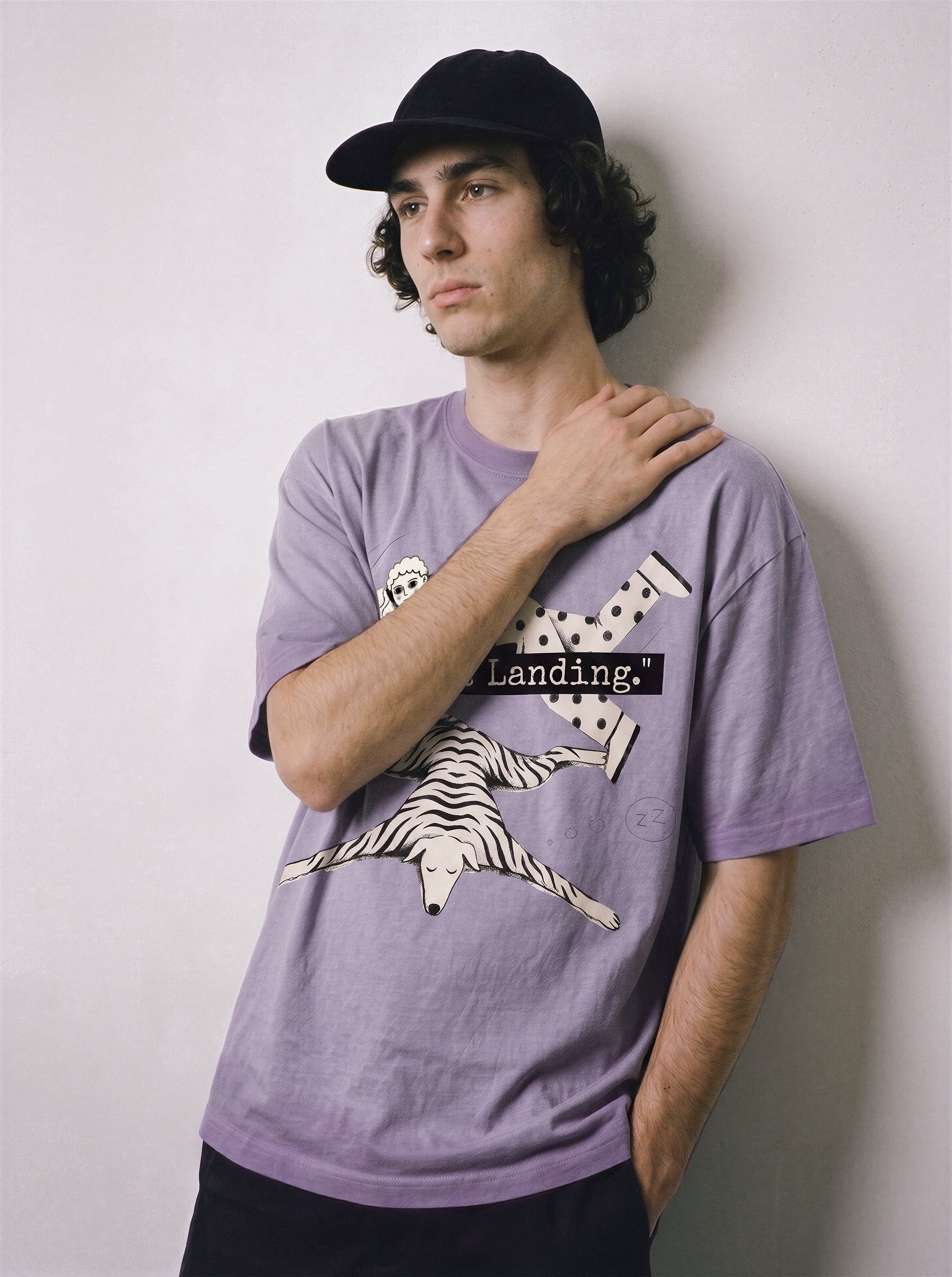 A male model touching his shoulder wearing an ombre violet face down soft landing graphic tee, highlighting the hitting the floor graphic and deadpan aesthetic.