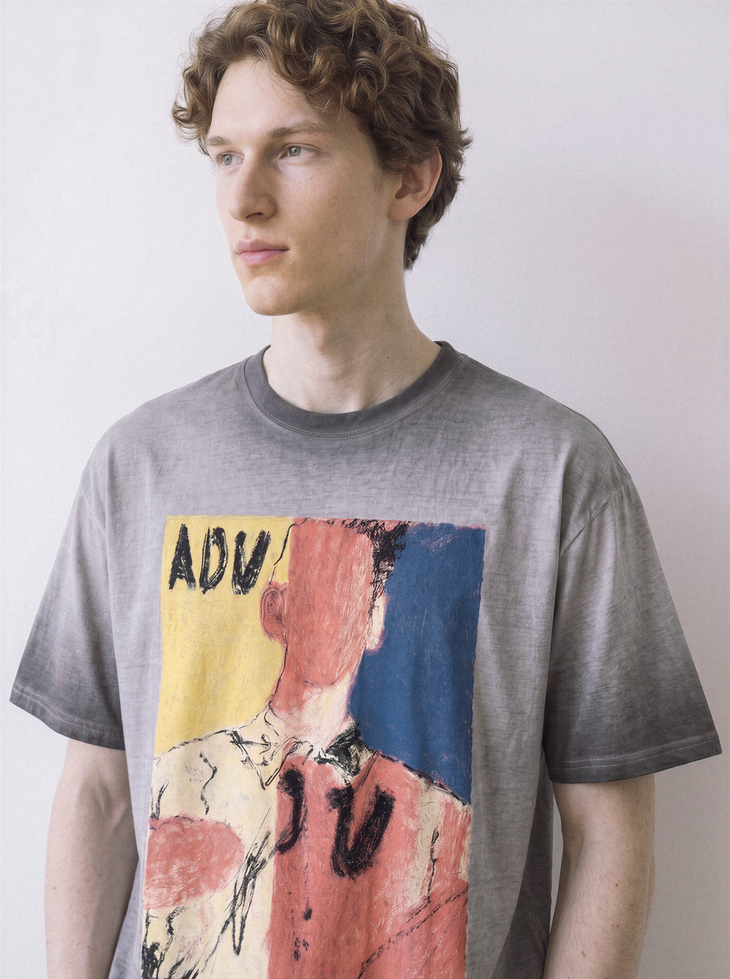 A front view of a male model looking aside wearing an ombre grey faceless portrait oil pastel graphic tee, displaying the high-contrast visual statement design.