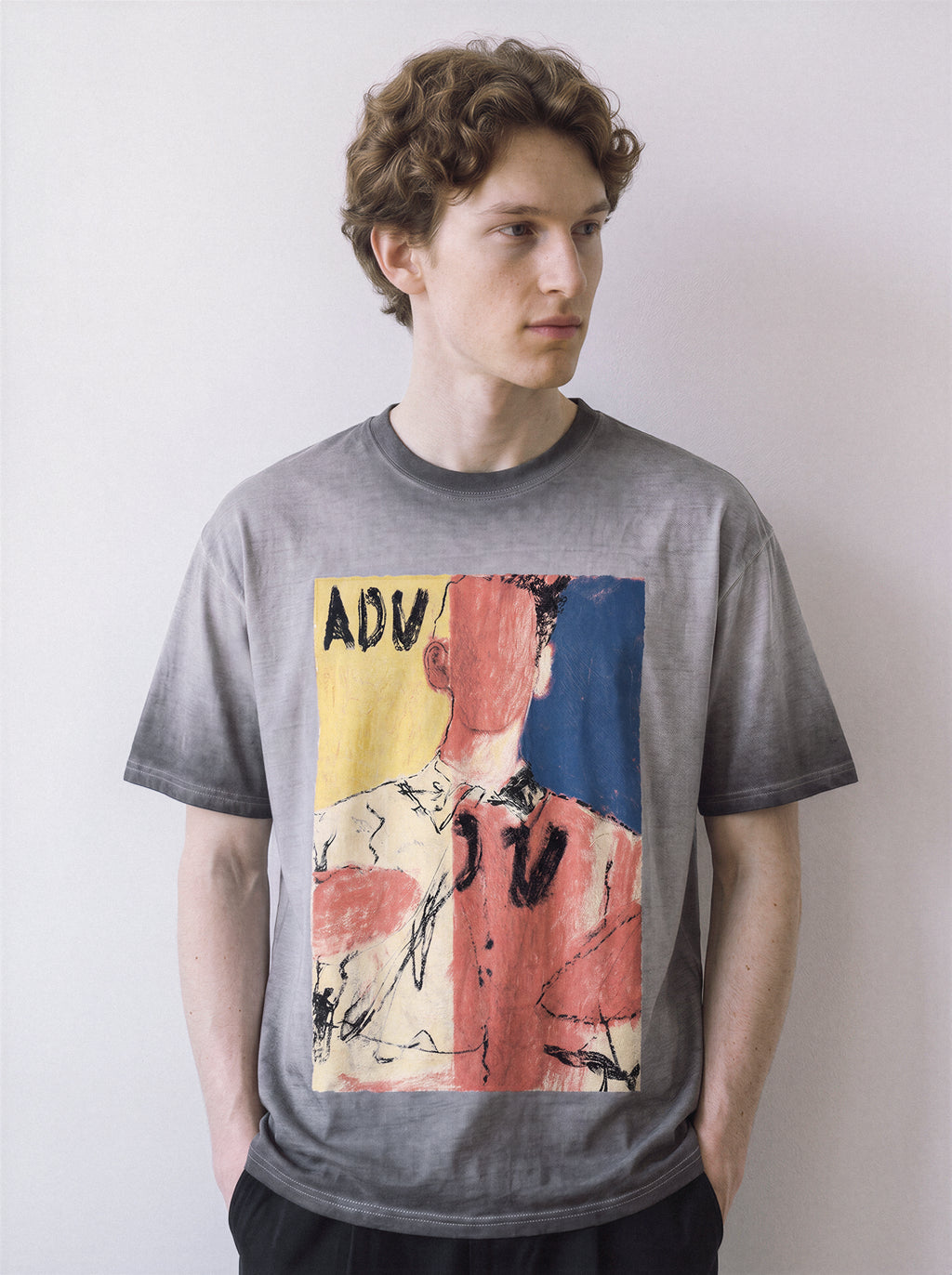 A front view of a male model looking to the right wearing an ombre grey faceless portrait oil pastel graphic tee, emphasizing the vivid primary color blocks and abstract identity streetwear vibe.