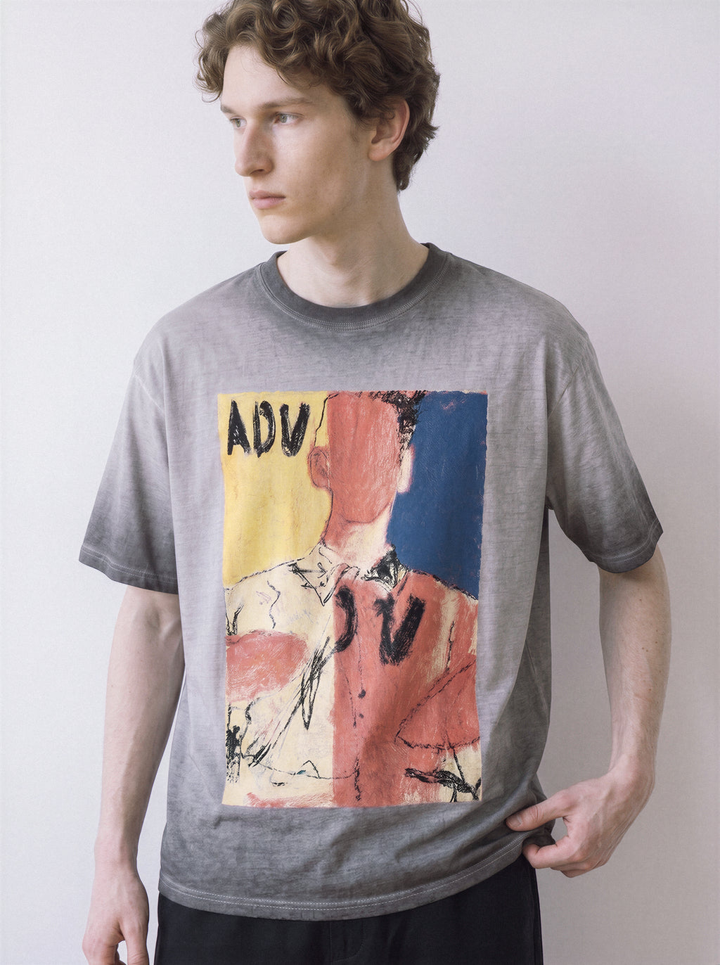 A side stance of a male model wearing an ombre grey faceless portrait oil pastel graphic tee, highlighting the unpolished execution and relaxed boxy fit.