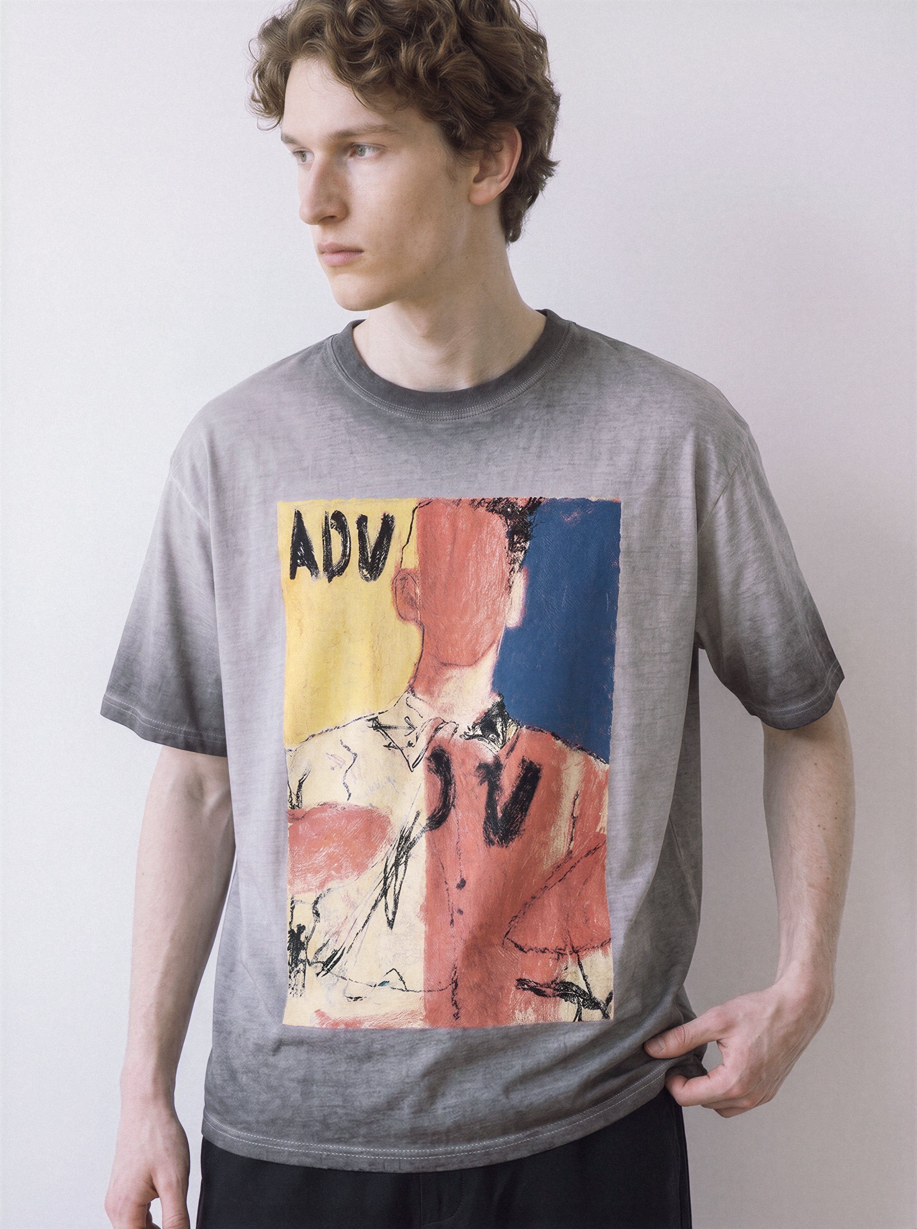 A side stance of a male model wearing an ombre grey faceless portrait oil pastel graphic tee, highlighting the unpolished execution and relaxed boxy fit.