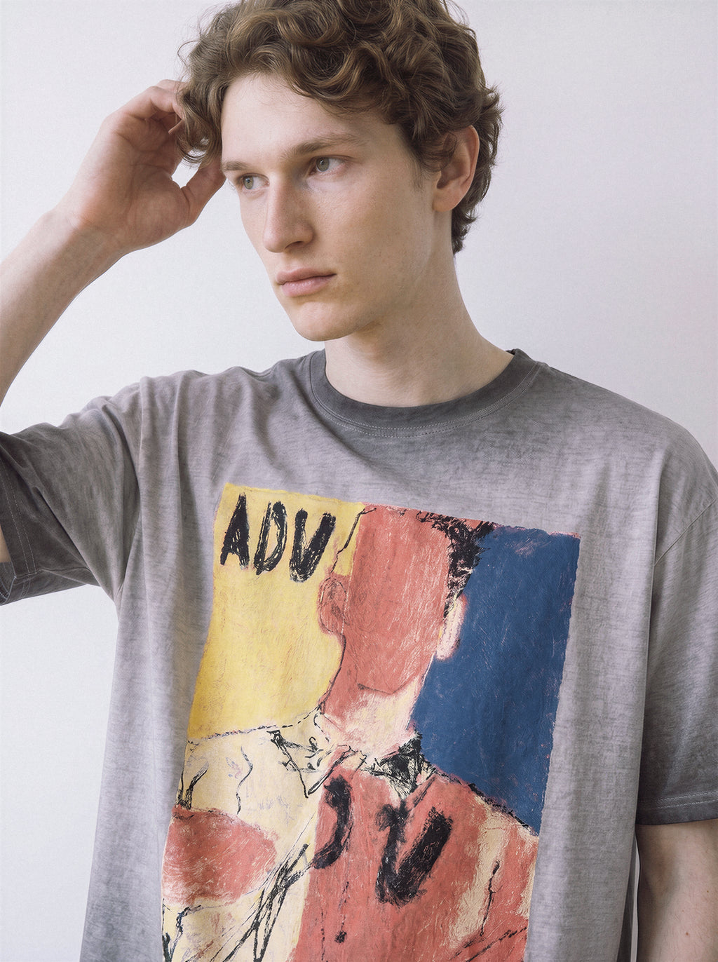 A close-up of a male model touching his head wearing an ombre grey faceless portrait oil pastel graphic tee, showcasing the heavy oil-pastel strokes and raw art aesthetic.