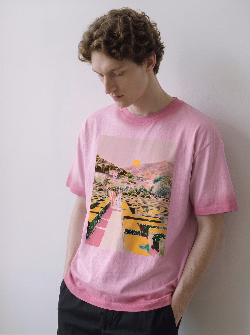 A male model looking down wearing an aura pink geometric labyrinth graphic novel tee, showcasing the high-saturation maze landscape print and relaxed boxy fit.