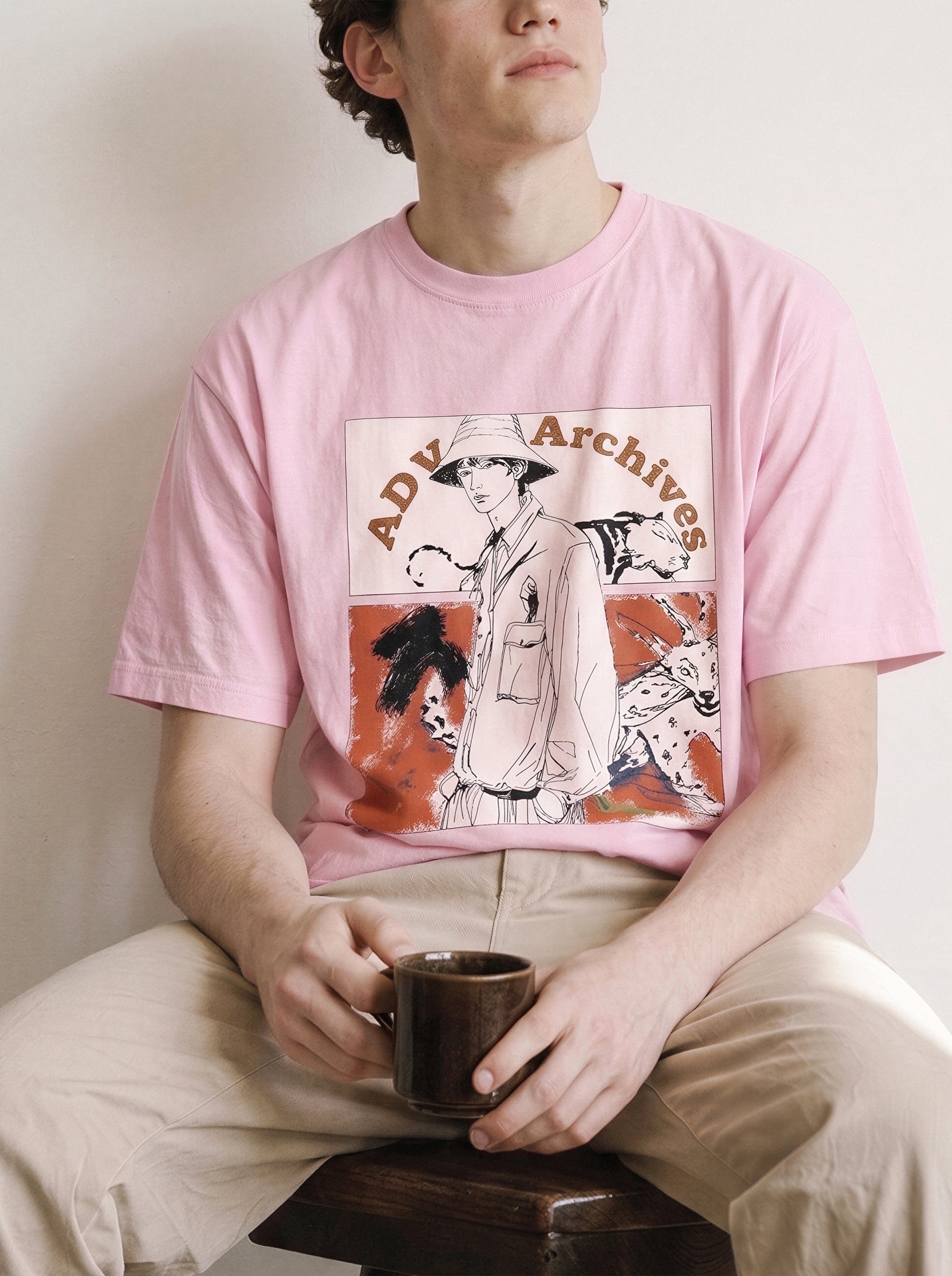 A seated male model looking up and away holding a mug wearing an aura pink graphic novel boy and wildlife tee, highlighting the raw sketch streetwear aesthetic and casual drape.