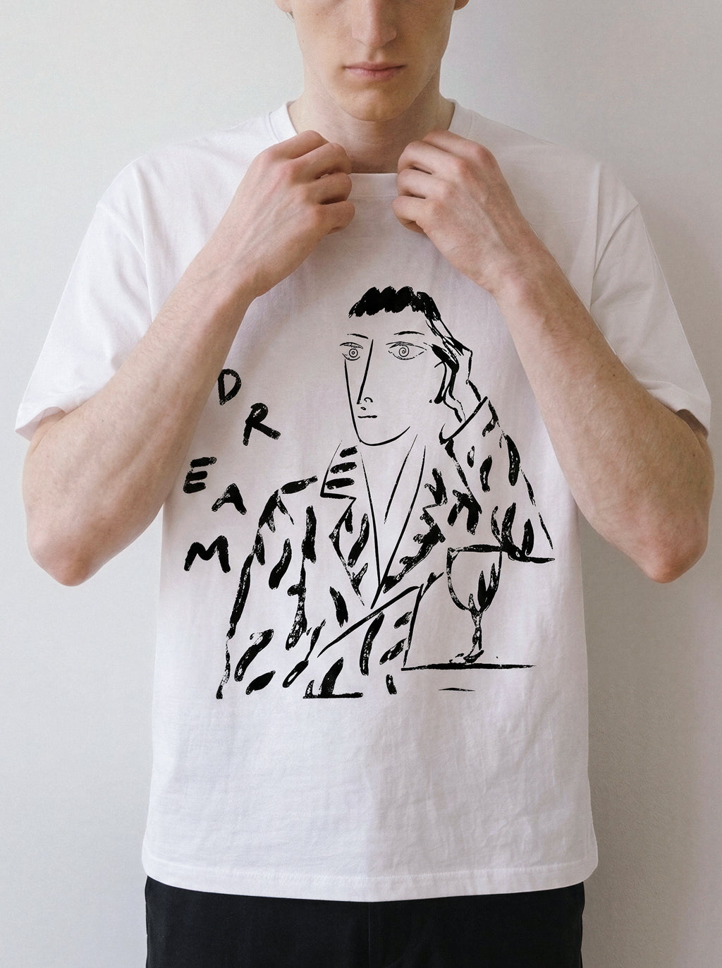A front view of a male model adjusting his collar wearing a white hand-lettered dream portrait line art graphic tee, highlighting the pure line art form and independent manga aesthetic.