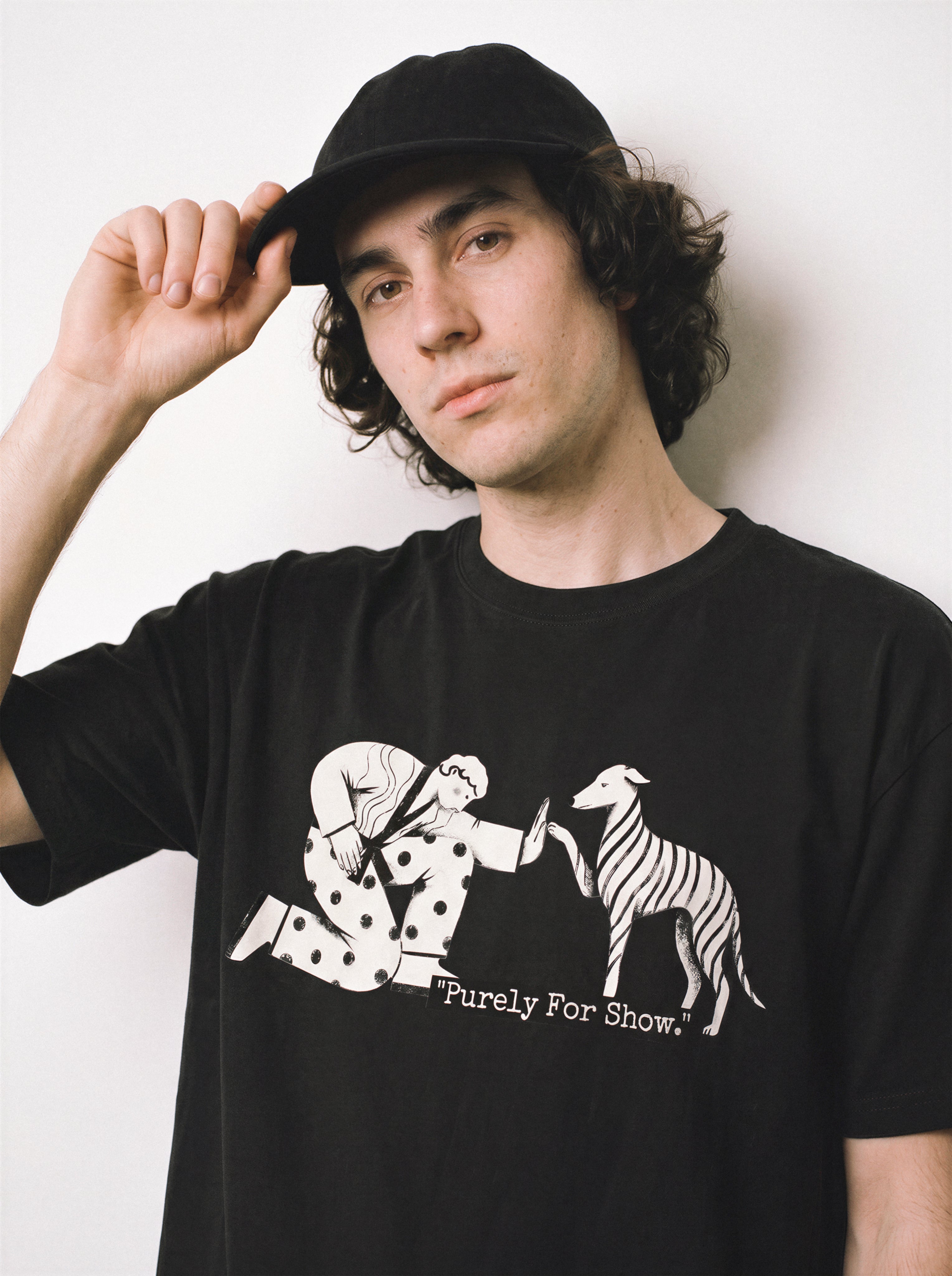 A close-up of a male model holding his cap wearing a black handshake gesture line art graphic tee, showcasing the formal handshake graphic and going through the motions vibe.