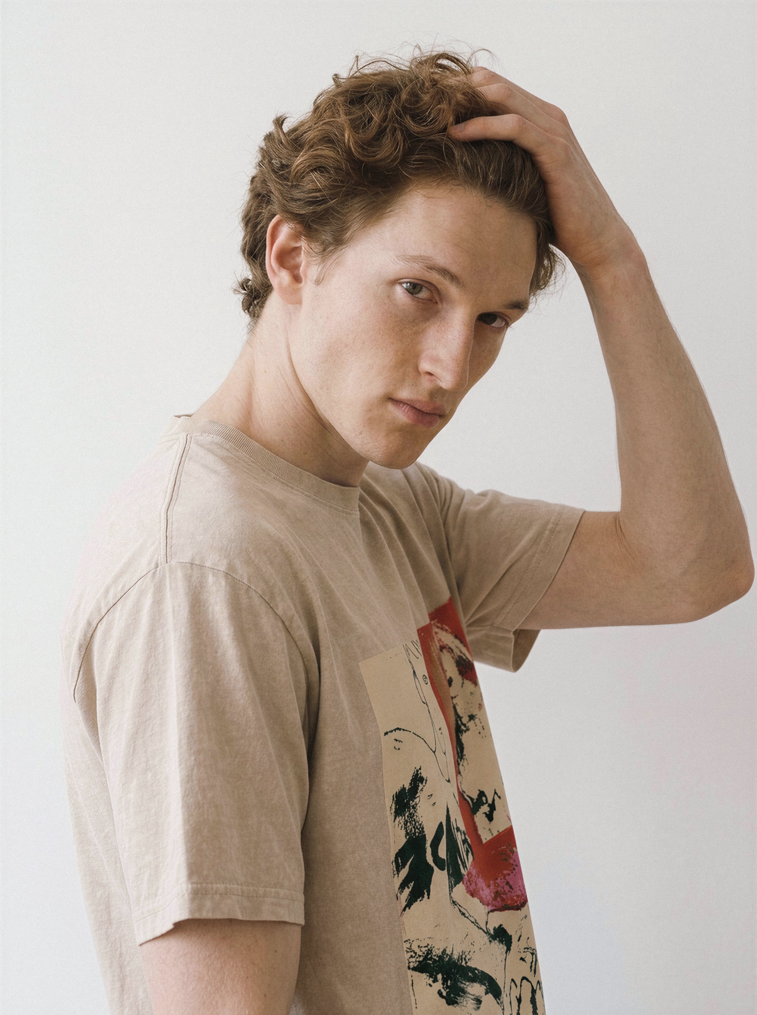 A male model with his hand in his hair wearing a mineral sand handshake portrait mixed media graphic tee, capturing the visual fragmentation and grunge art style.