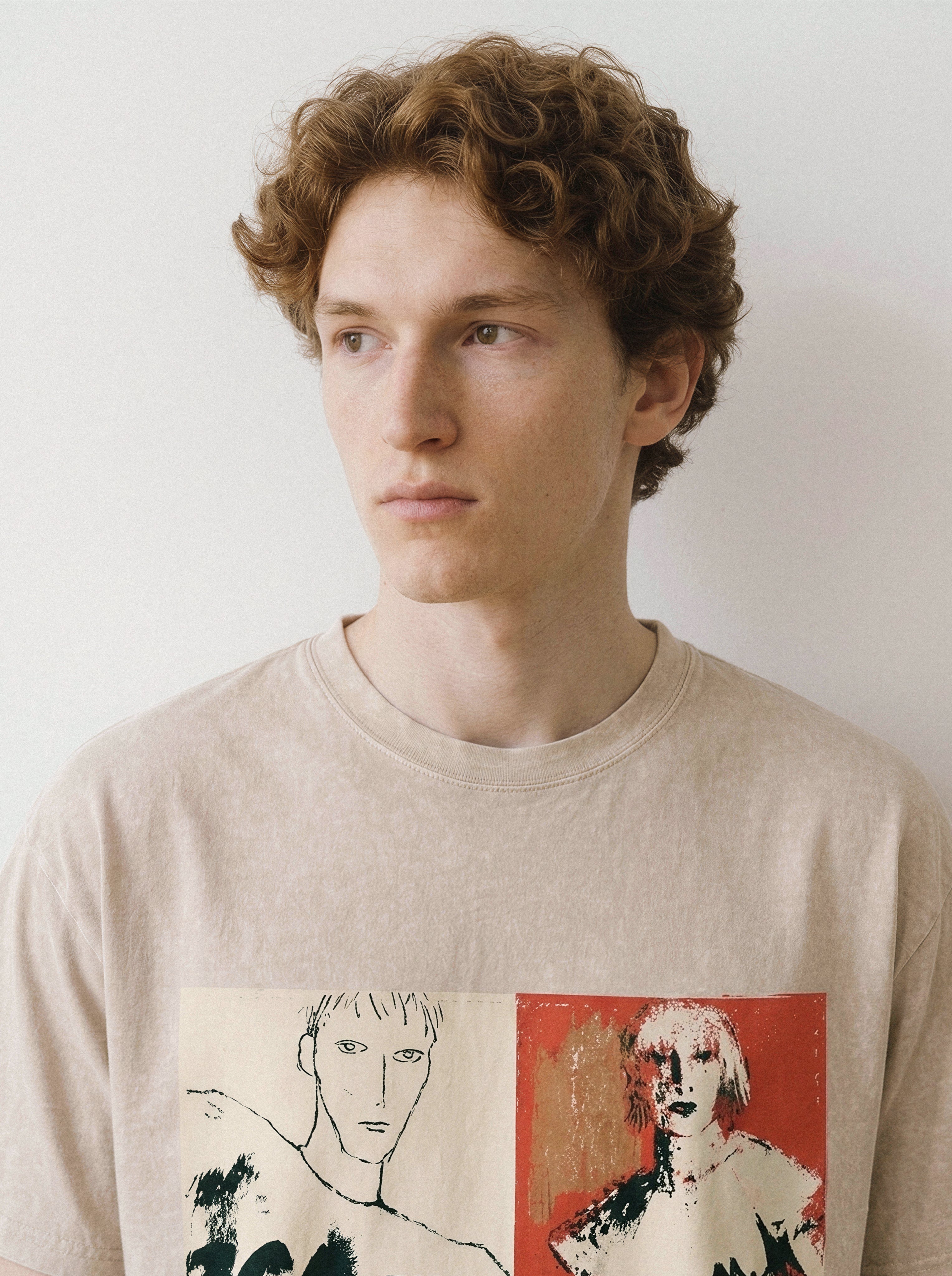 A close-up of a male model looking aside wearing a mineral sand handshake portrait mixed media graphic tee, highlighting the raw portrait sketches and unspoken tension design.