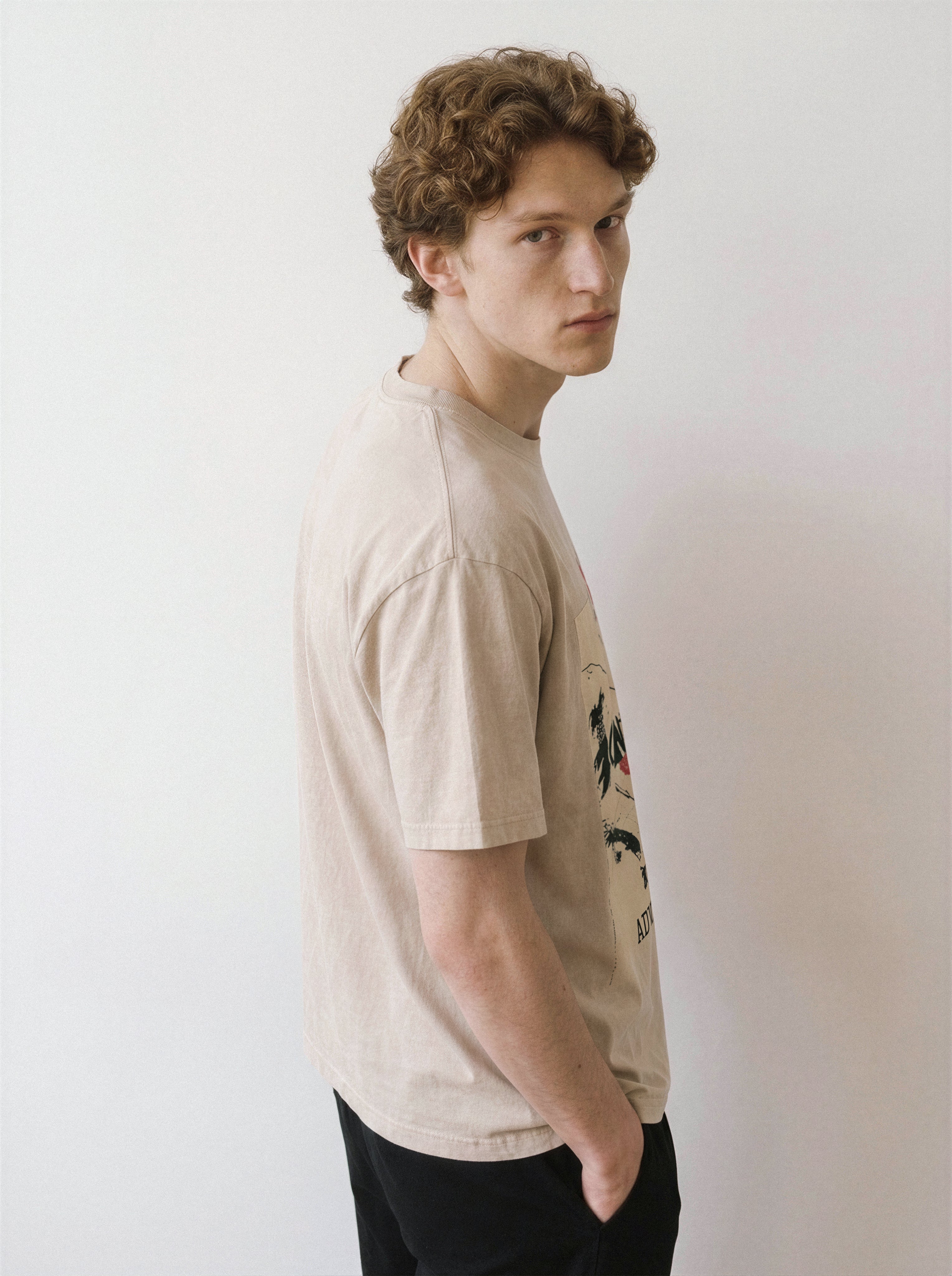 A male model looking over his shoulder wearing a mineral sand handshake portrait mixed media graphic tee, displaying the bold color blocks and raw streetwear aesthetic.