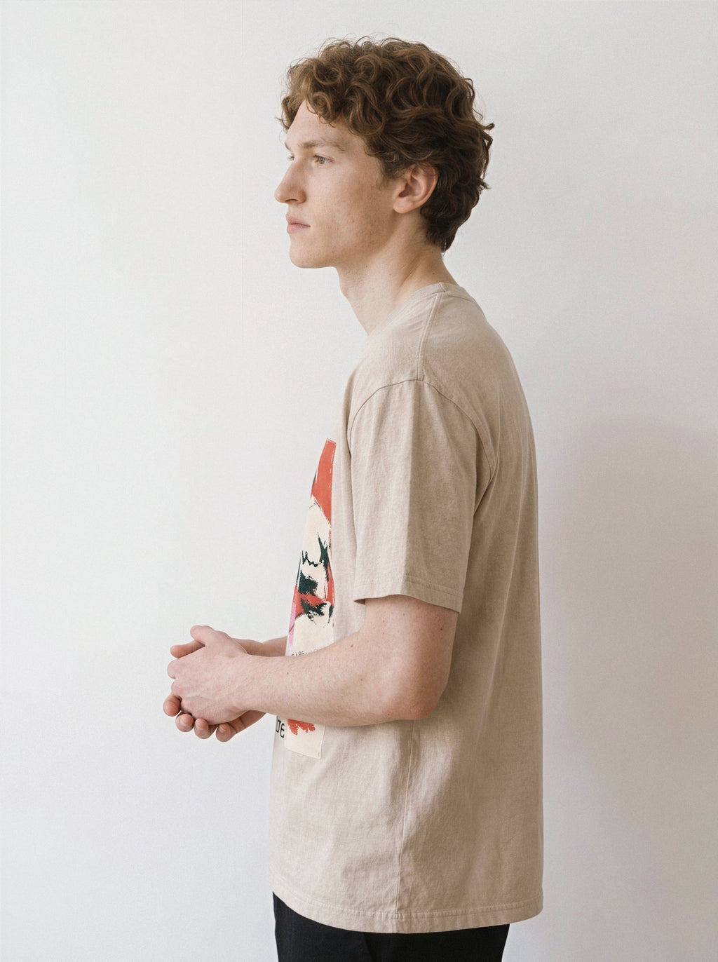 A side profile of a male model with hands clasped wearing a mineral sand handshake portrait mixed media graphic tee, showcasing the unpolished execution and relaxed boxy fit.