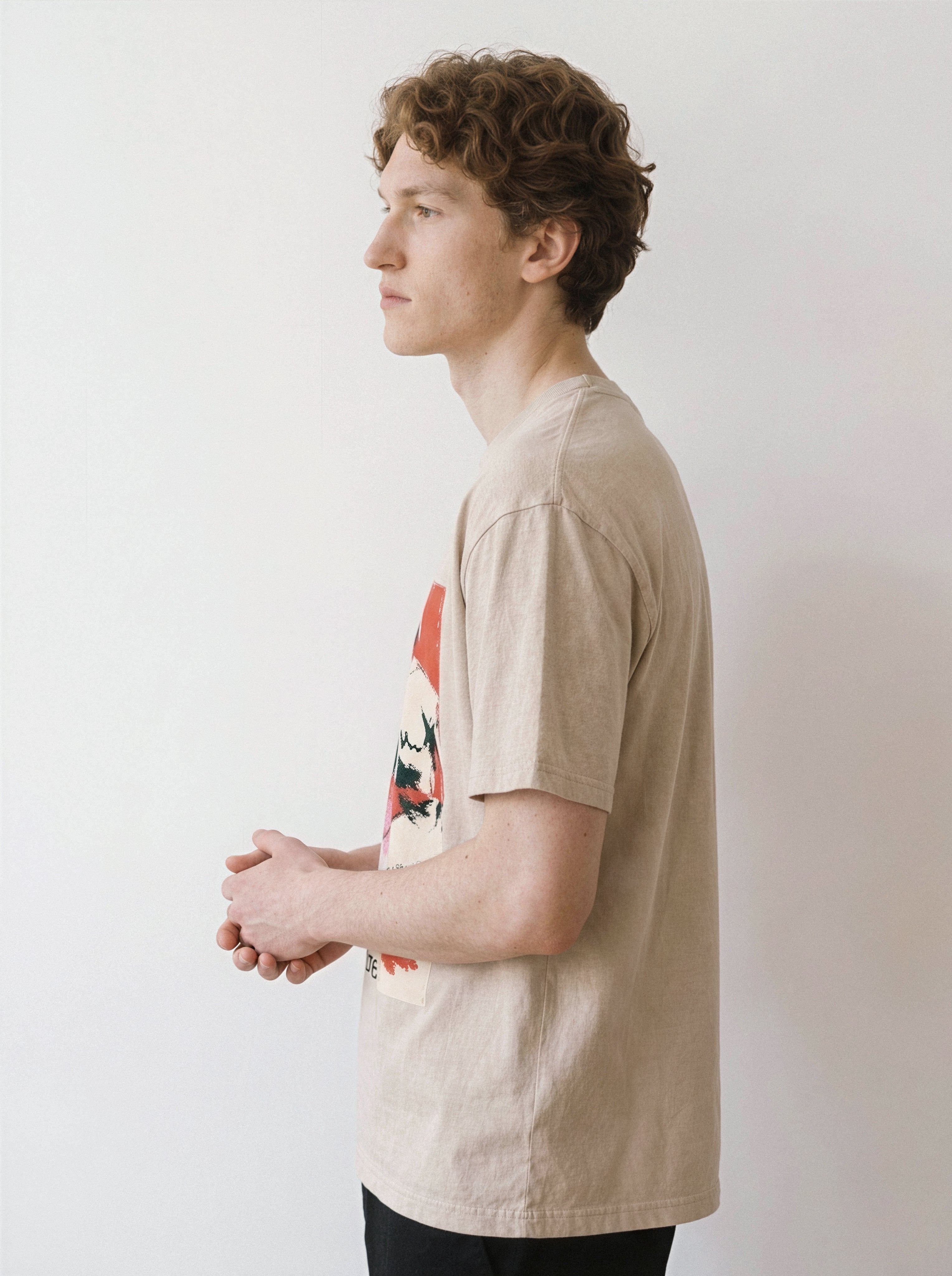 A side profile of a male model with hands clasped wearing a mineral sand handshake portrait mixed media graphic tee, showcasing the unpolished execution and relaxed boxy fit.